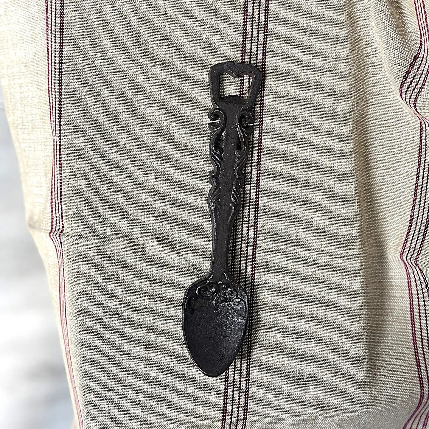 Decorative black spoon bottle opener on a textured fabric background