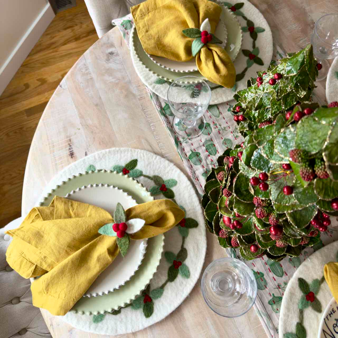 Decorative table setting with greenery and yellow napkins on a round table.