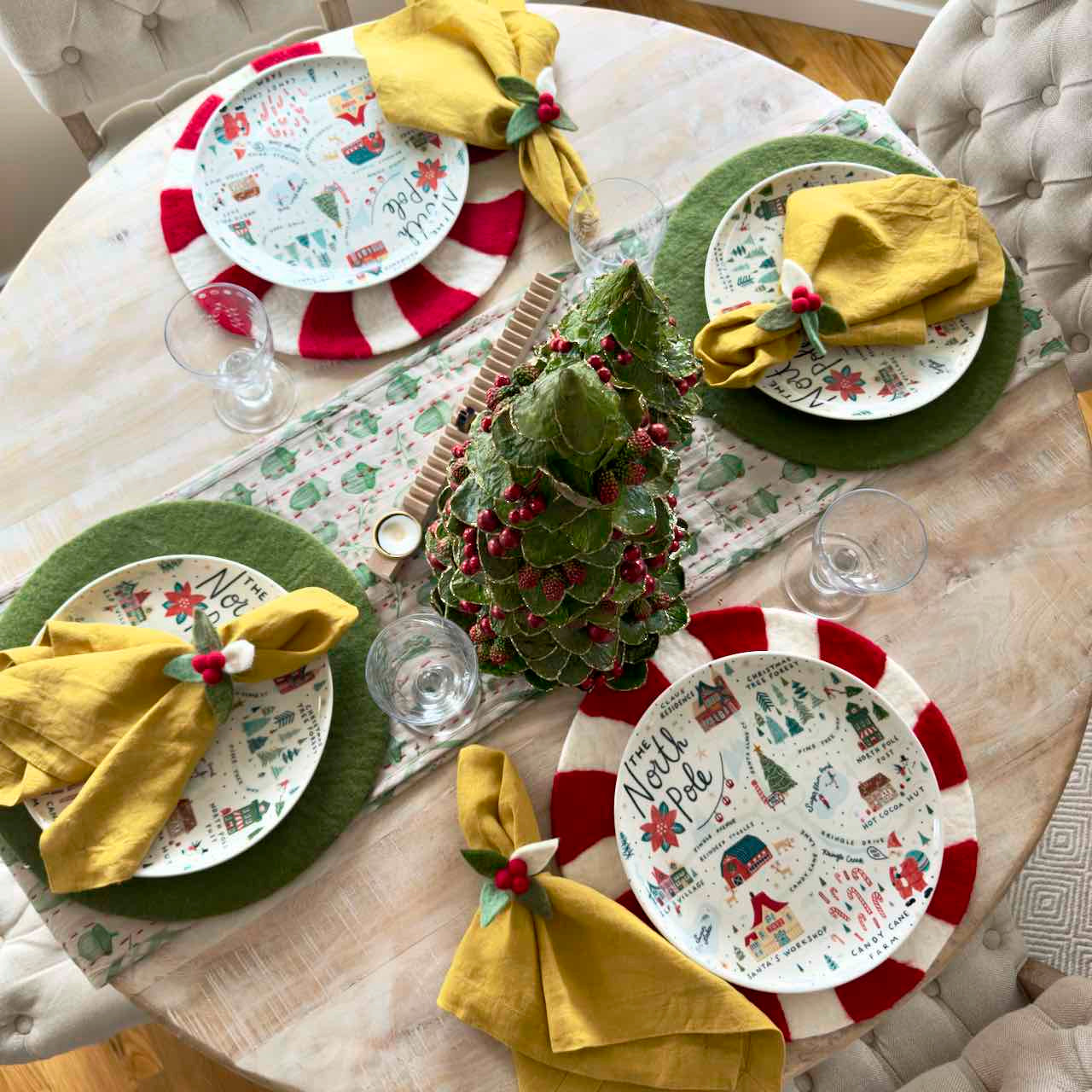Decorative Christmas table setting with plates, napkins, and a small tree on a round table.