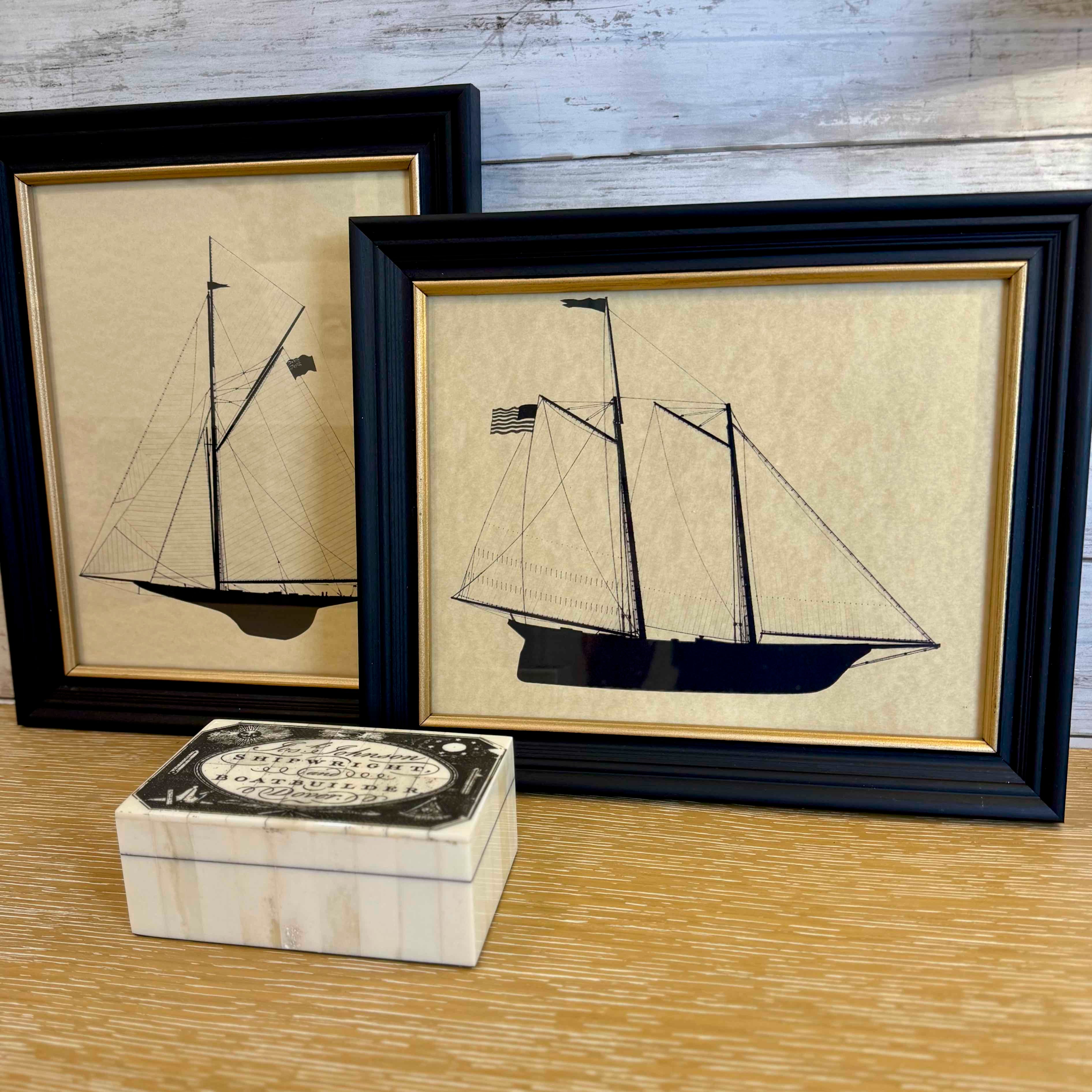 Two framed illustrations of ships on a wooden surface with a decorative box.