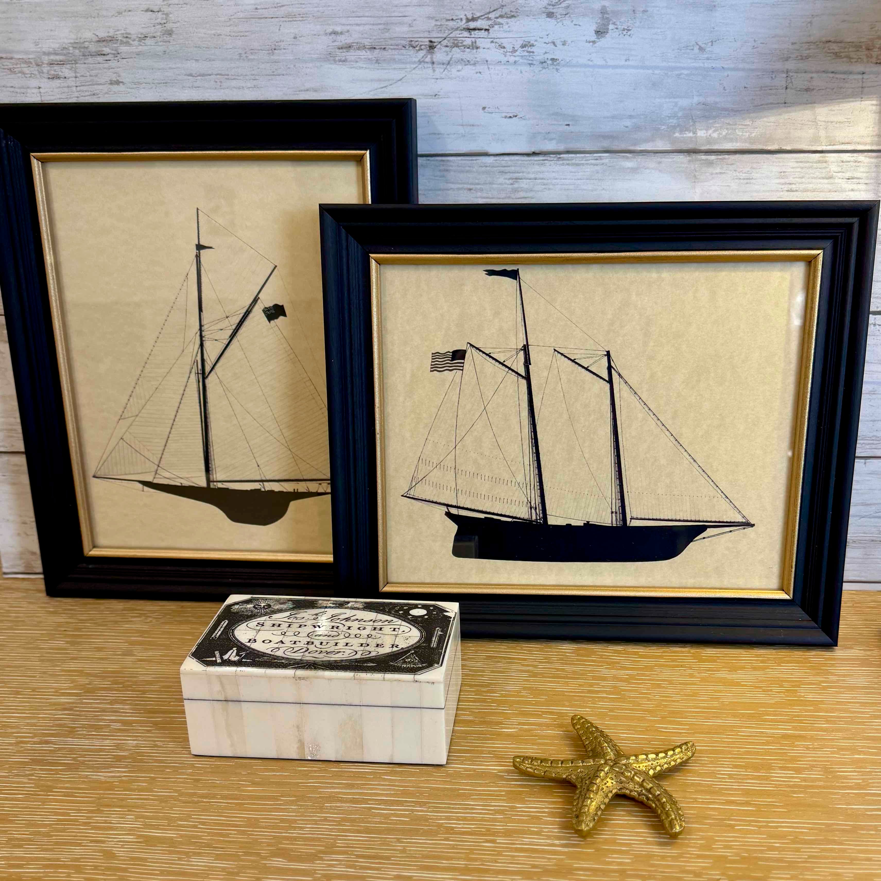 Two framed illustrations of ships on a wooden surface with a decorative box and starfish.