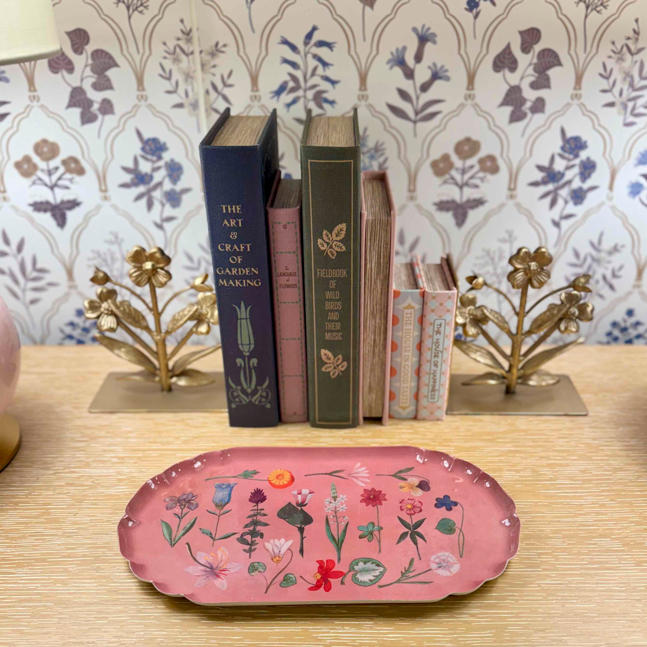 Decorative pink tray with floral designs on a table with books and decorative objects.