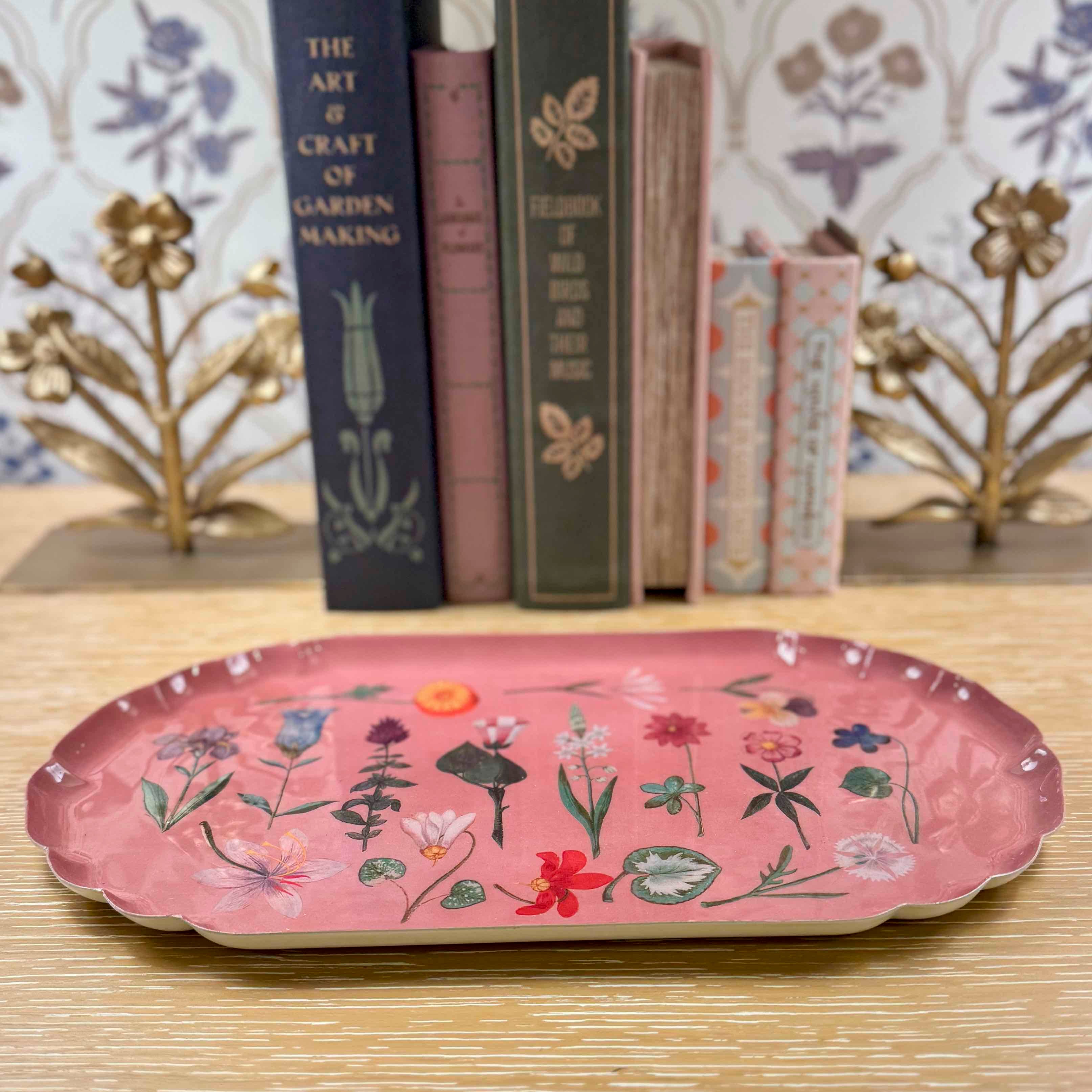 Pink decorative tray with floral designs on a wooden surface with books in the background