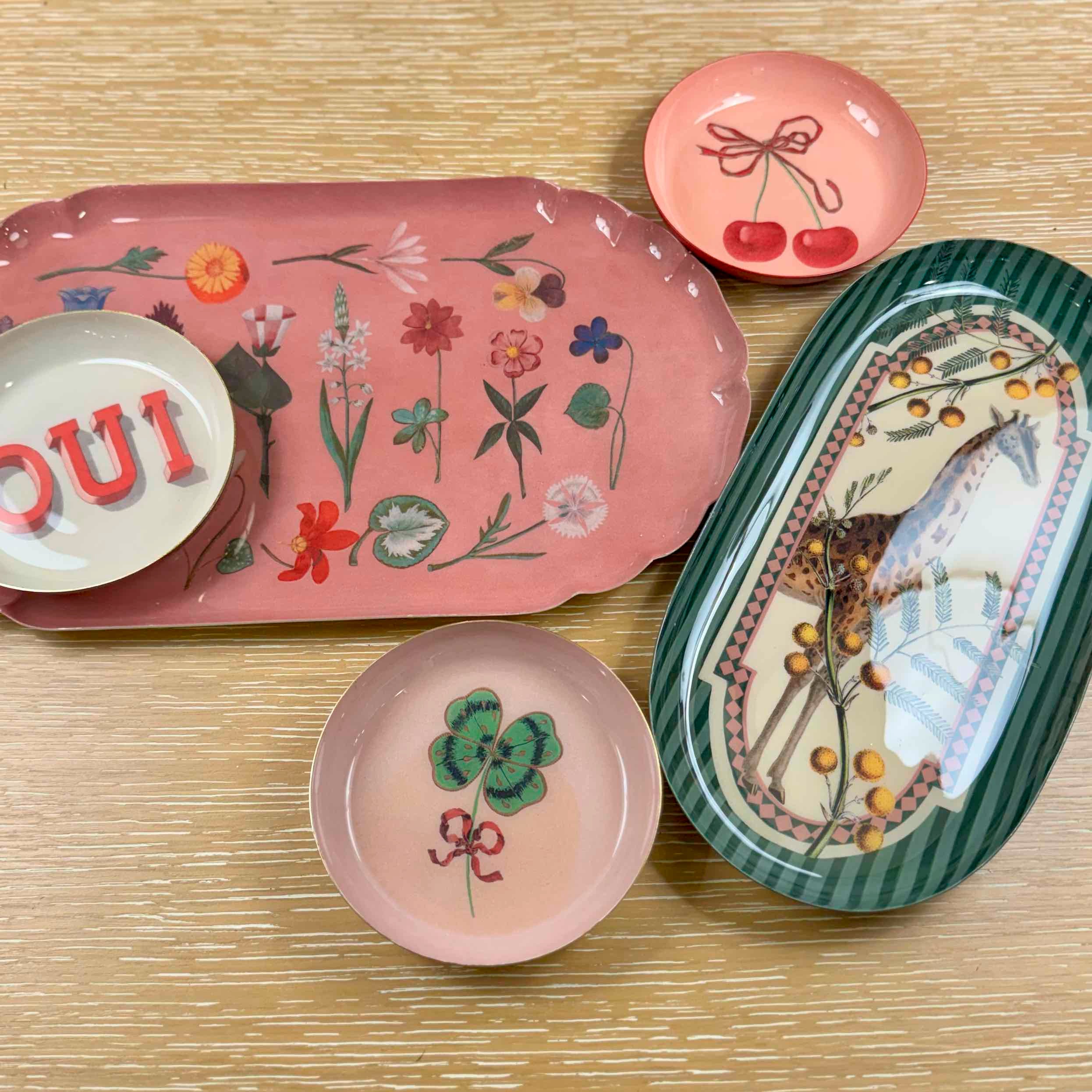 Collection of decorative plates and trays with floral and nature-themed designs on a wooden surface.