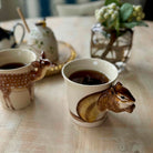 Two mugs with animal-shaped handles on a table with a blurred background