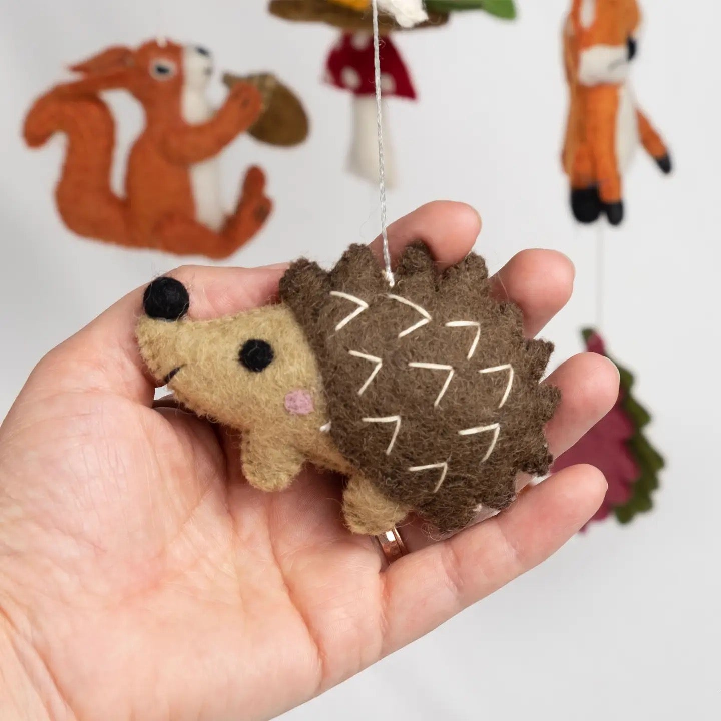 Hand holding a small hedgehog plush toy with a blurred background of other animal toys.