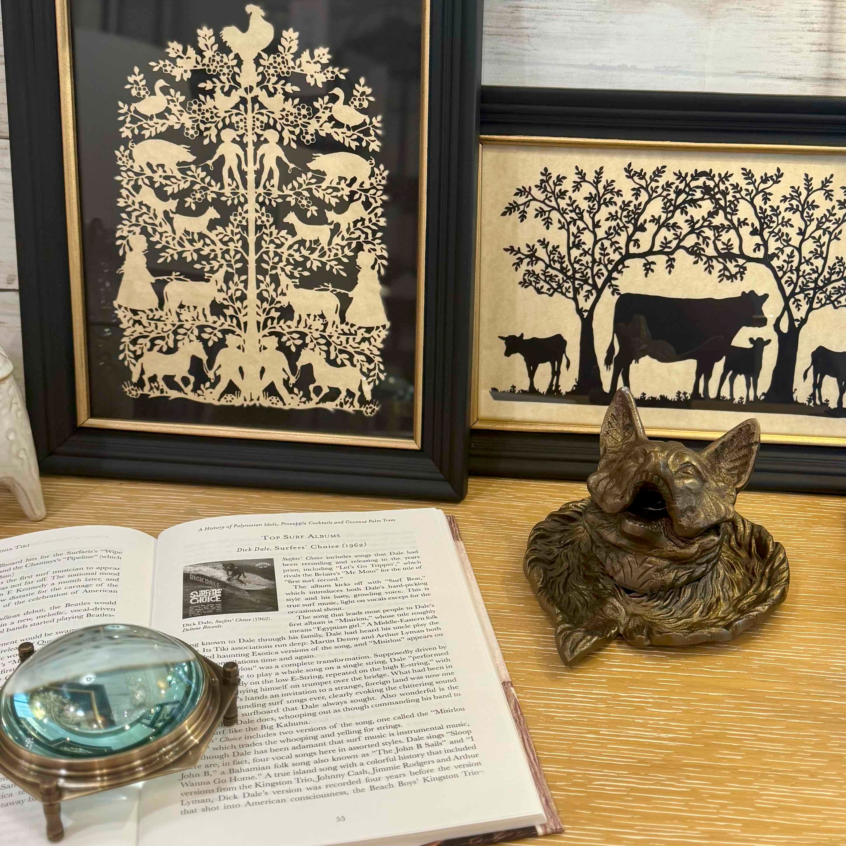 Framed papercut art of animals on a table with an open book and magnifying glass.