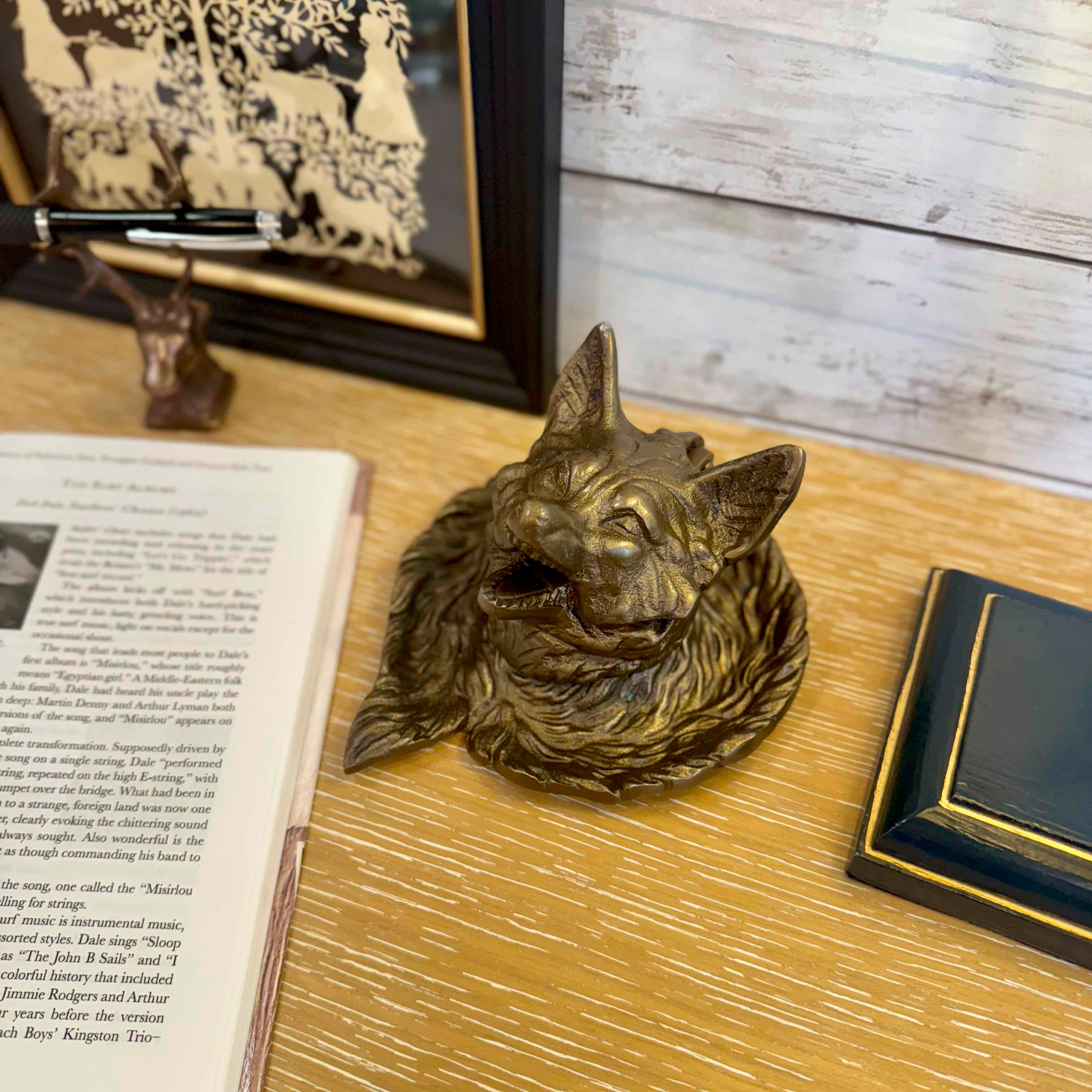 Bronze wolf head sculpture on a wooden surface with books and a framed picture in the background.