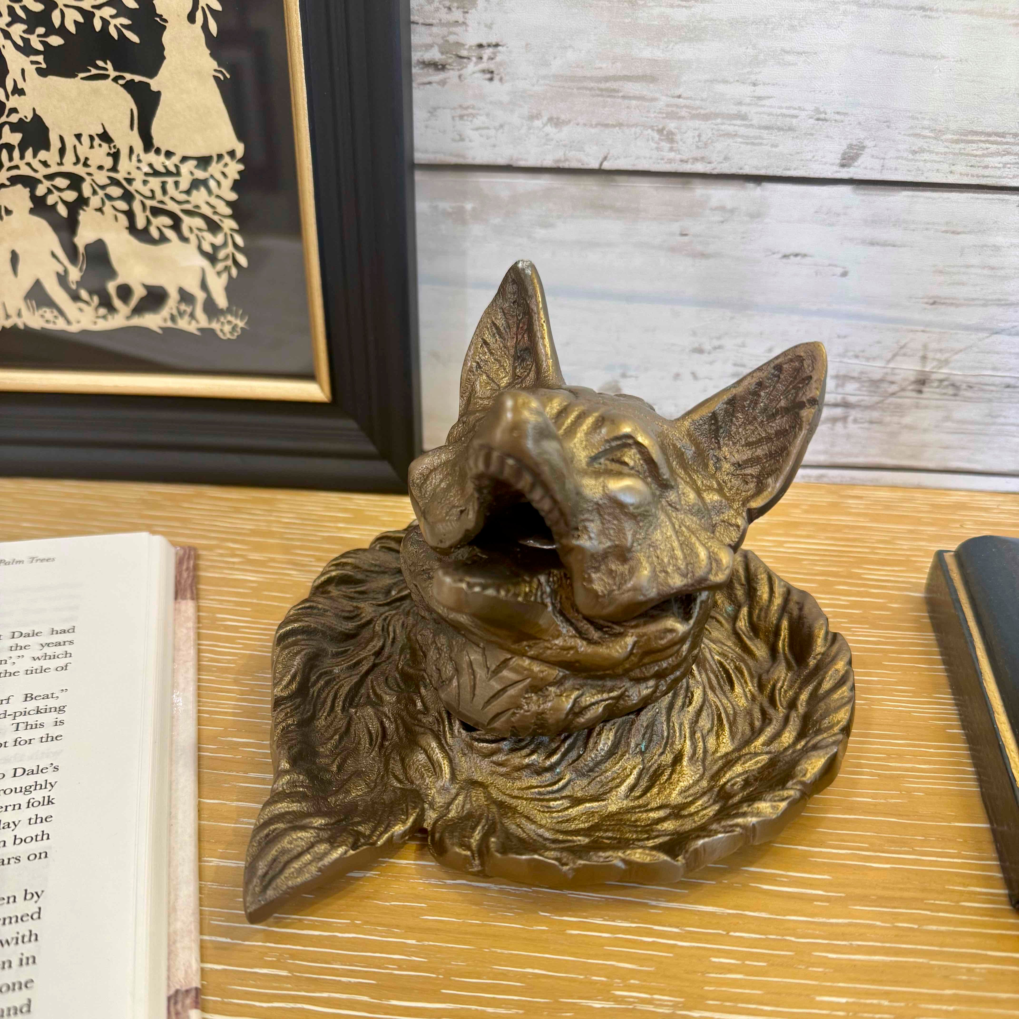 Bronze dog head sculpture on a wooden surface with a framed picture and book in the background.