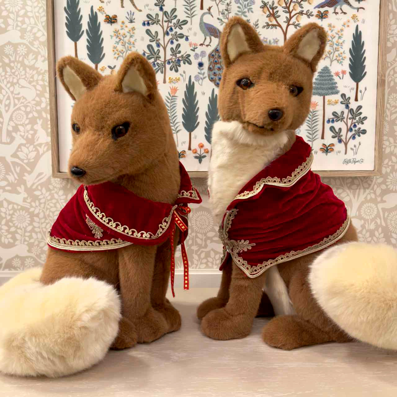 Two plush fox toys wearing red outfits with white lace details against a decorative wall.