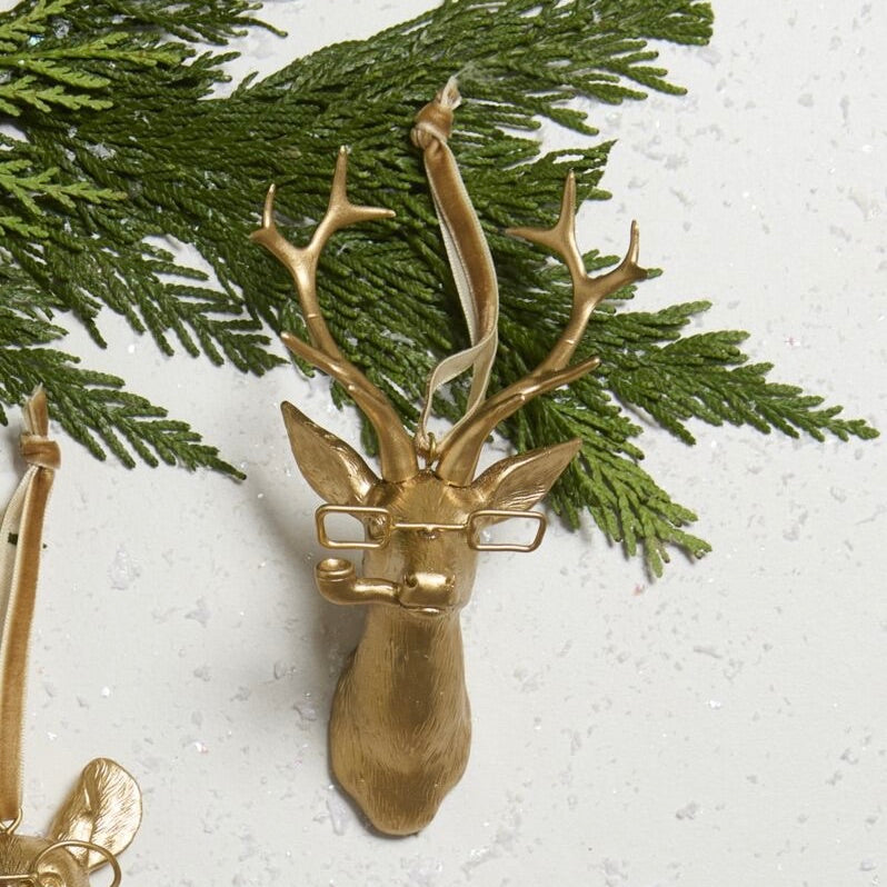 Gold deer head ornament with antlers on a white background with greenery