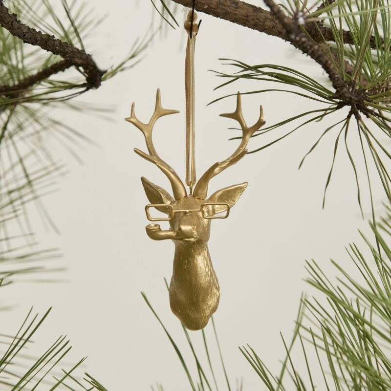 Gold deer ornament with glasses hanging from a pine branch