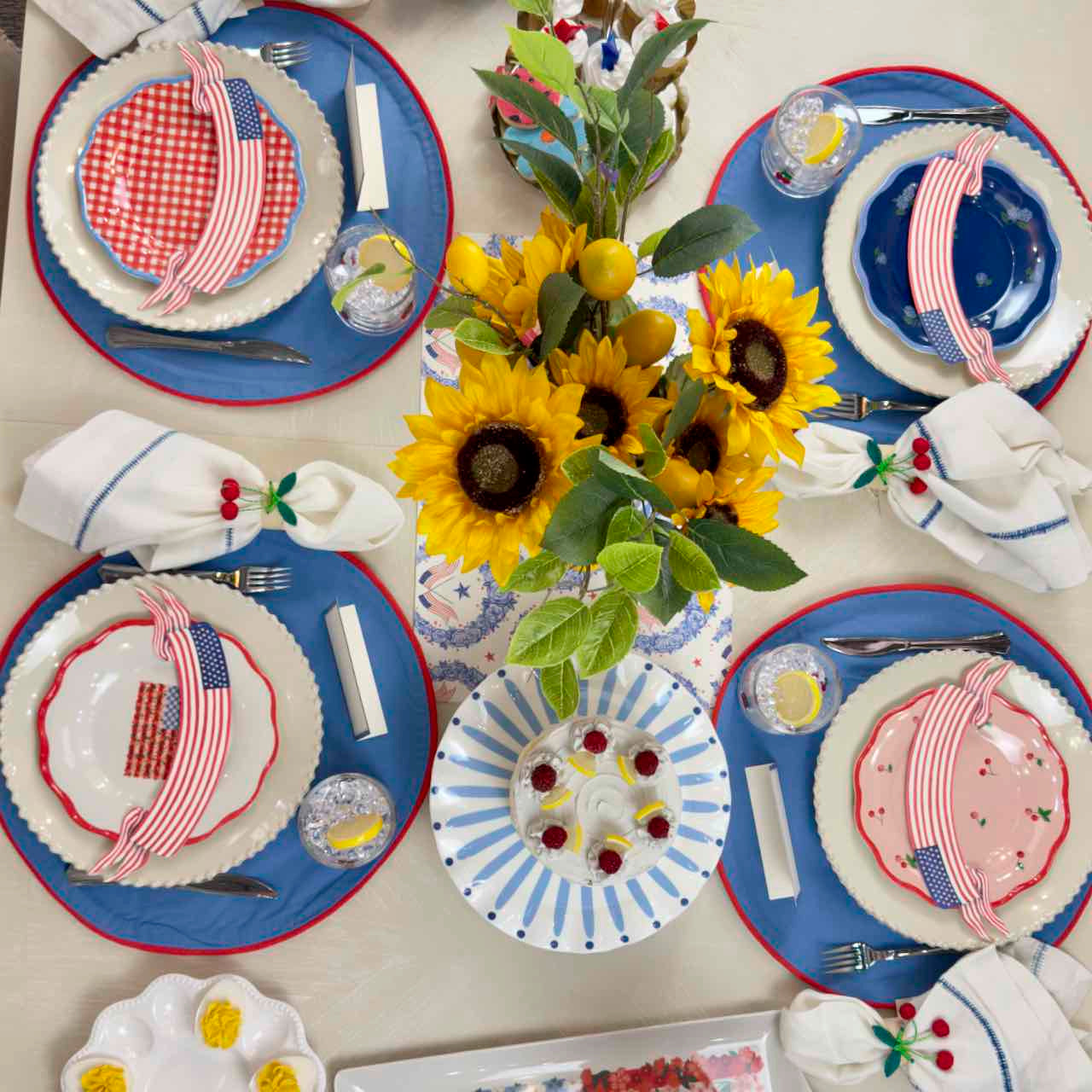 Dining table set with red, white, and blue plates, napkins, and sunflower centerpiece.
