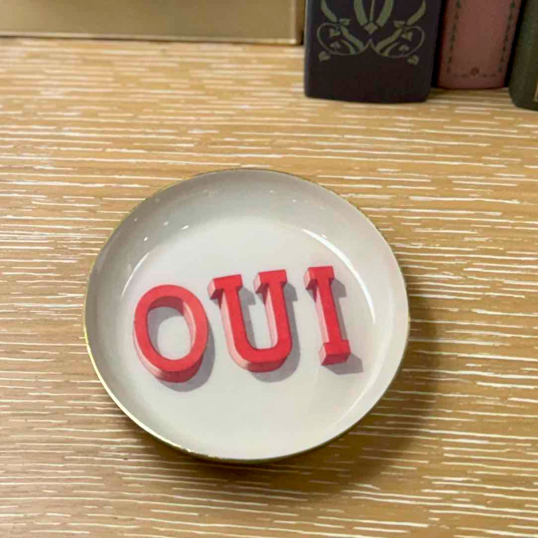 Round white plate with red 'OUI' text on a wooden surface