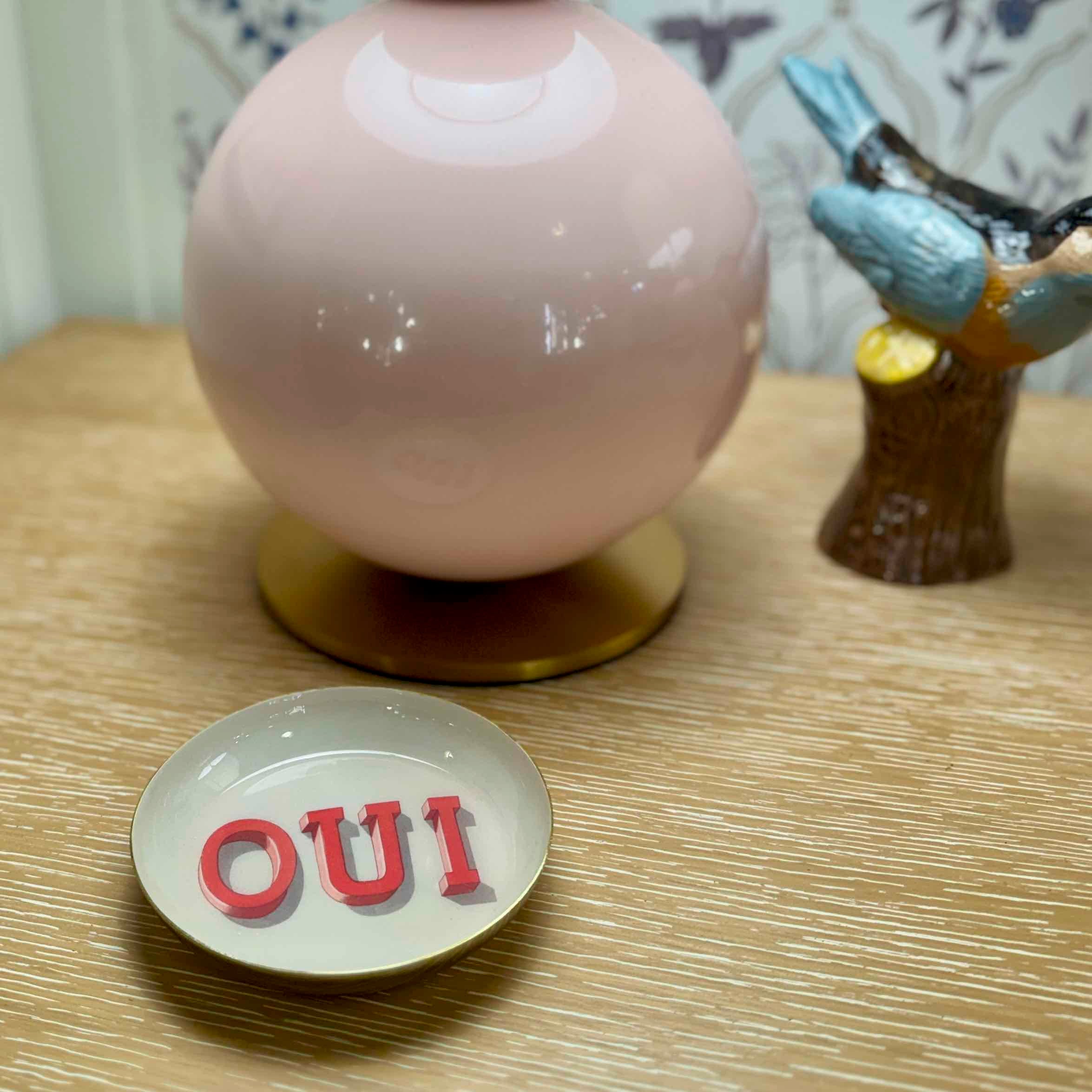 Pink spherical object on a stand with 'OUI' on a small plate on a wooden surface.