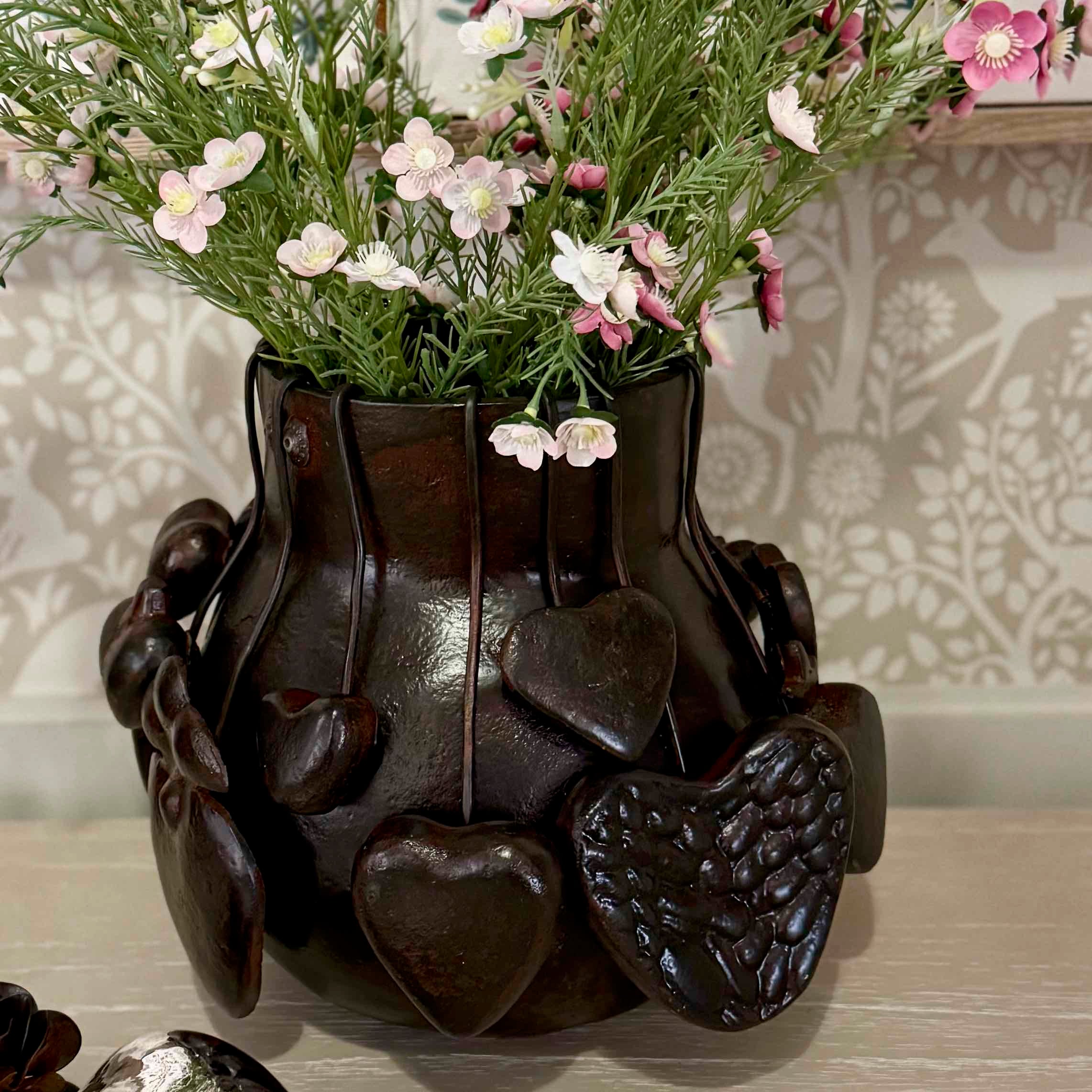 Decorative vase with heart designs holding flowers on a patterned wall background