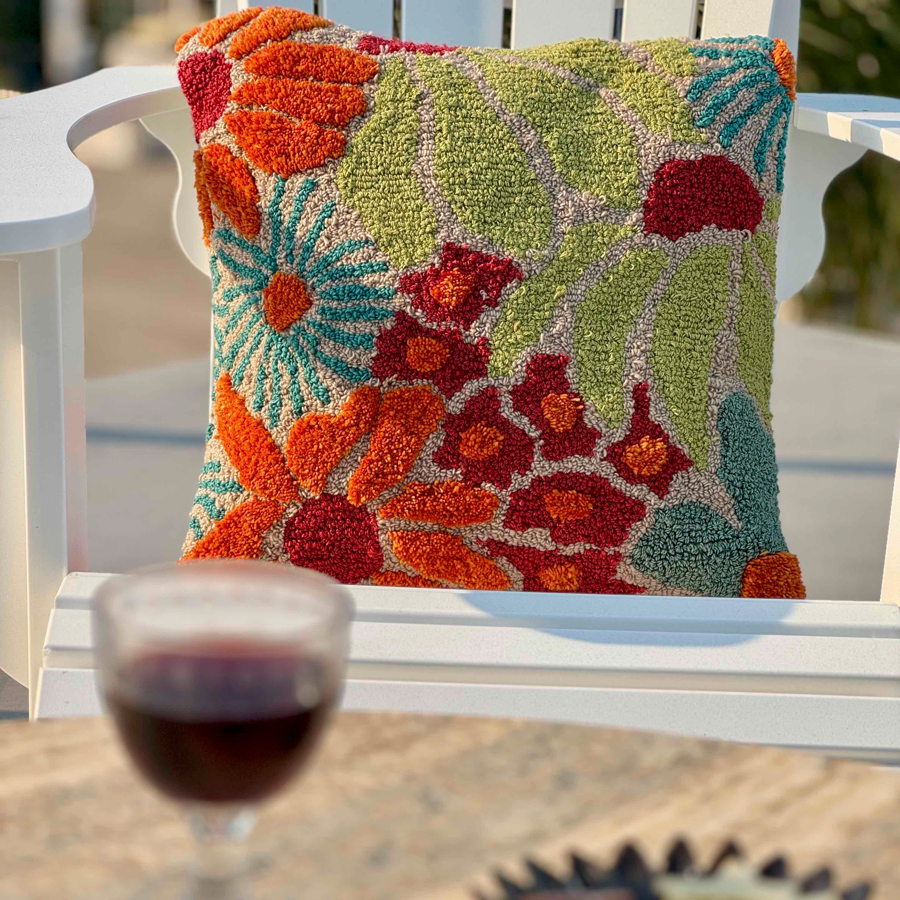 Decorative floral pillow on a chair with a glass of red wine in the foreground.