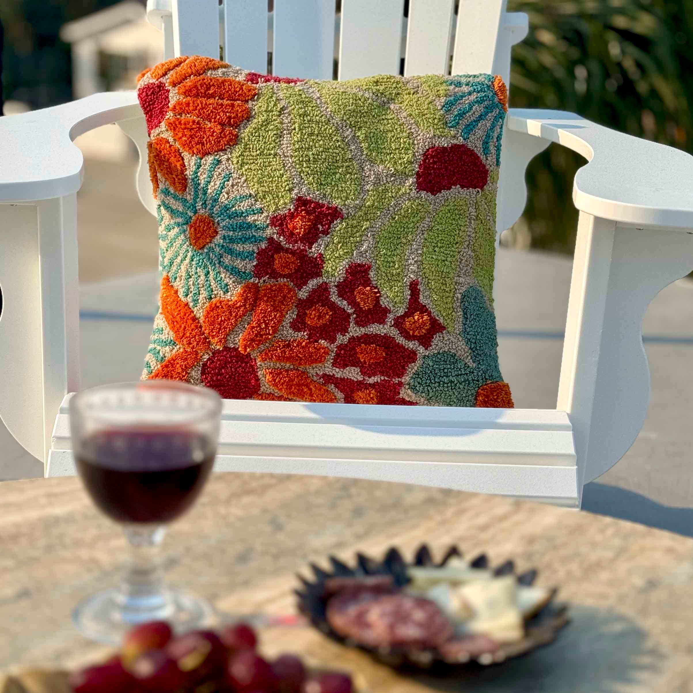 Colorful floral-patterned pillow on a white chair with a glass of red wine and snacks on a table.