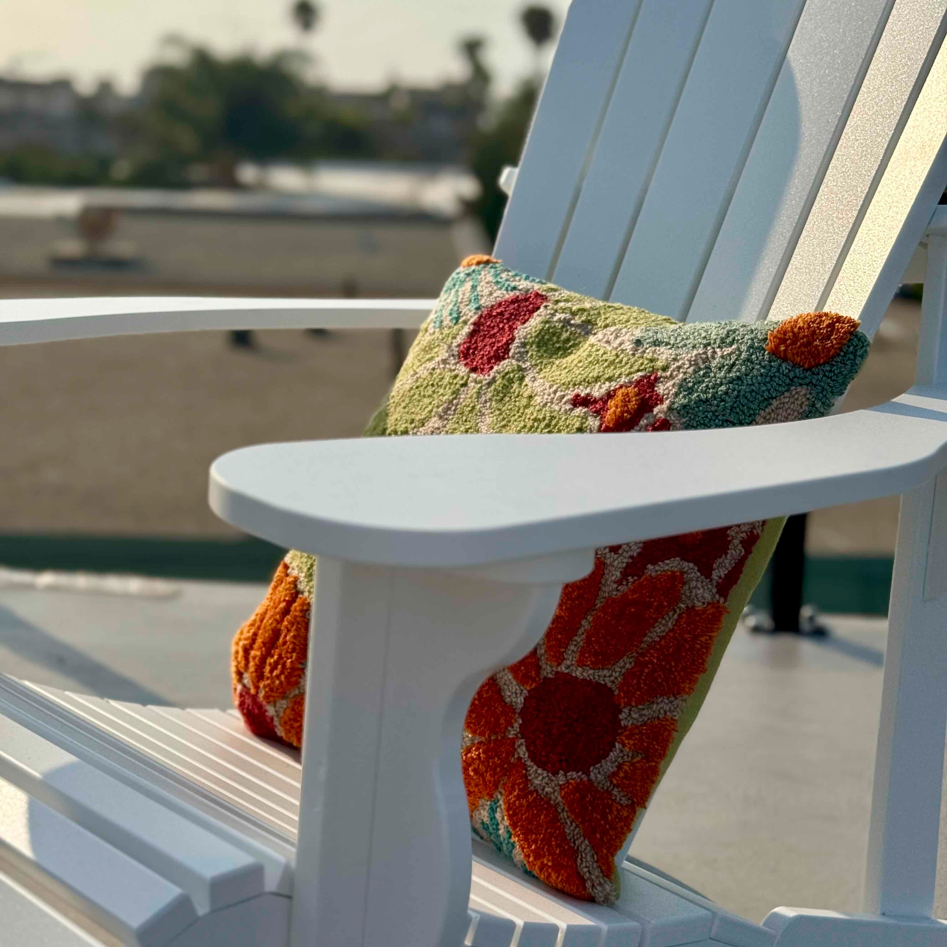 White Adirondack chair with a colorful patterned pillow on a blurred outdoor background