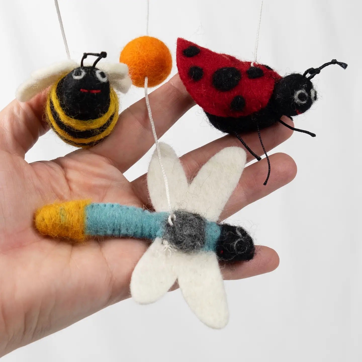 Hand holding three felt insect toys against a white background