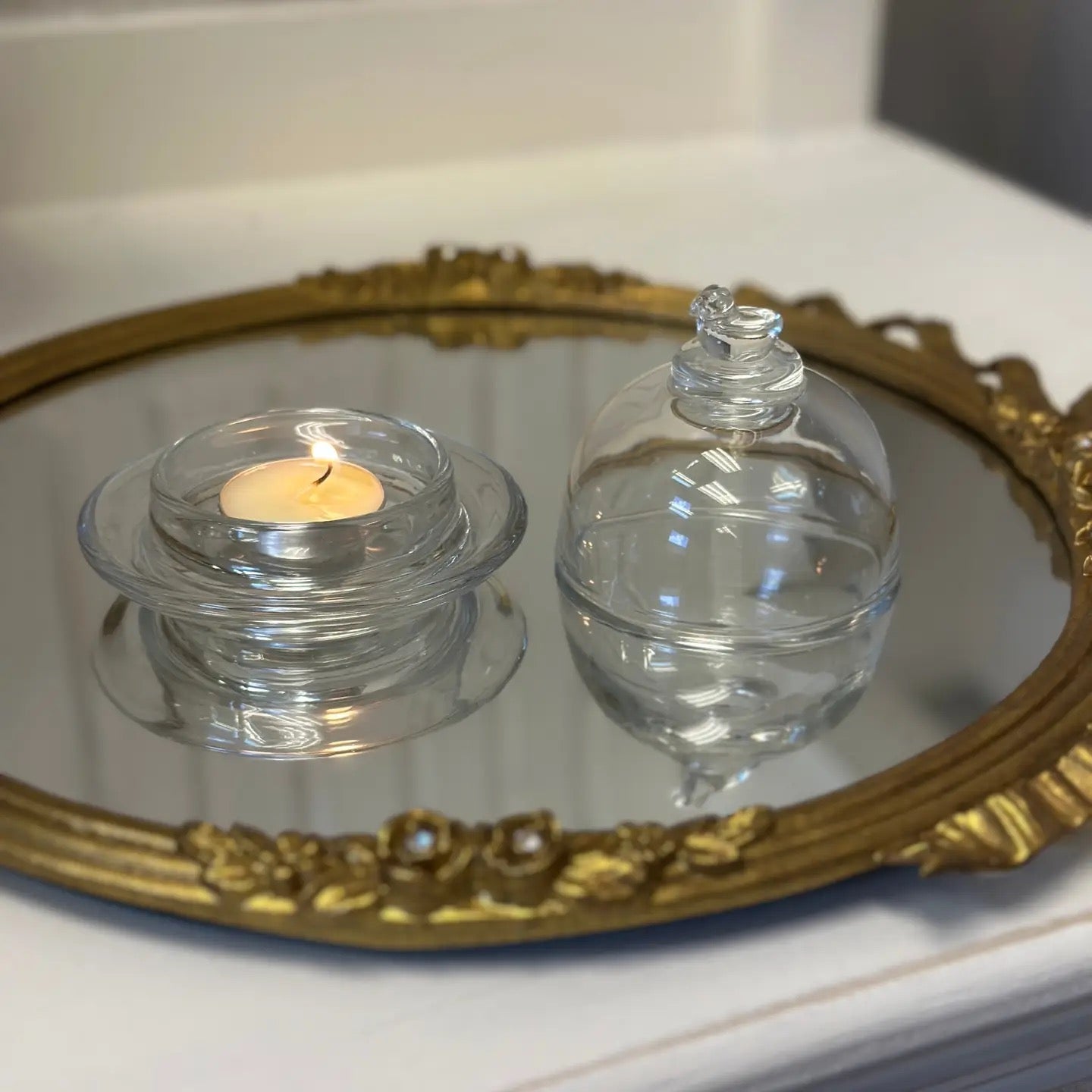 Two glass containers with a lit candle on a decorative mirror