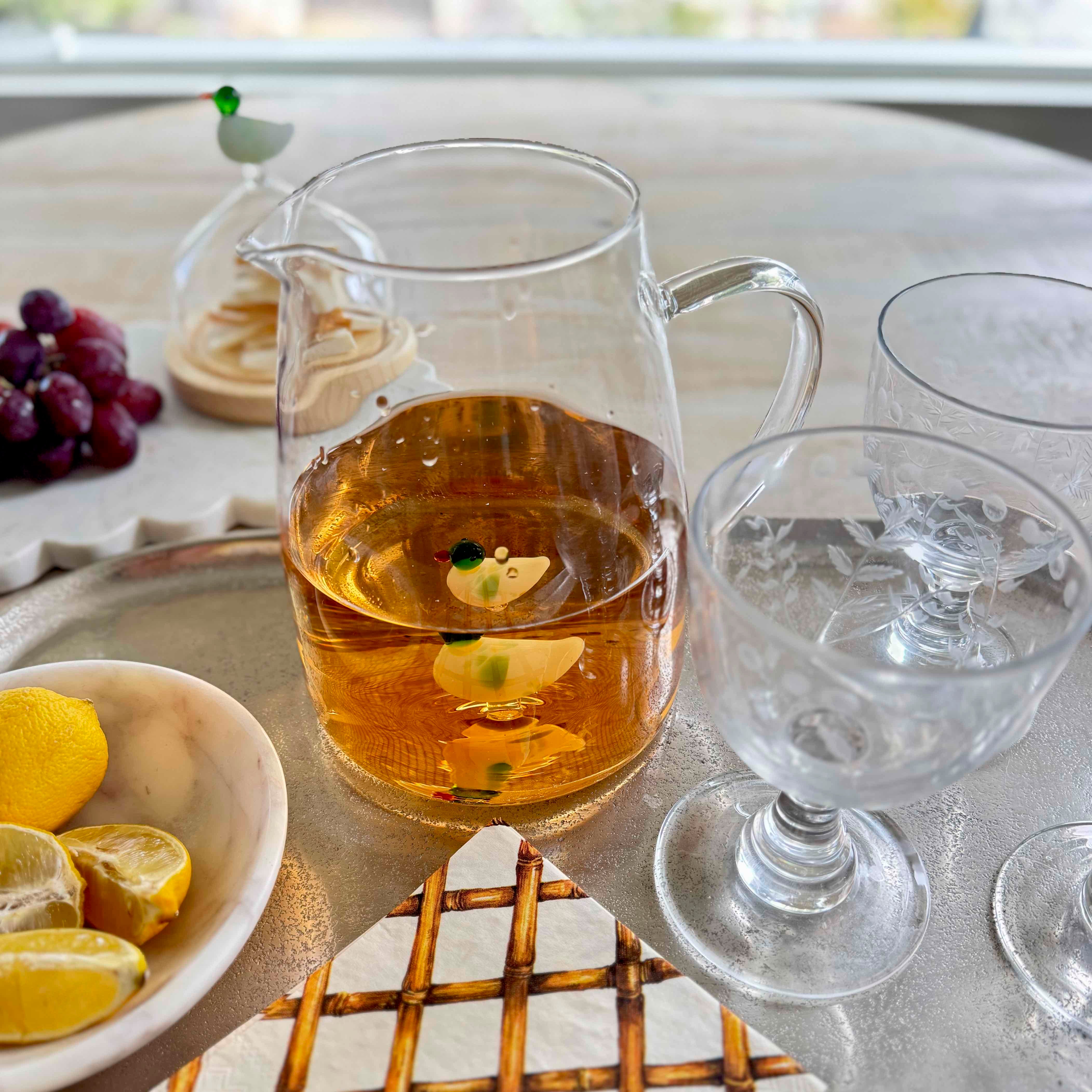 Glass pitcher with liquid on a table with lemons and grapes
