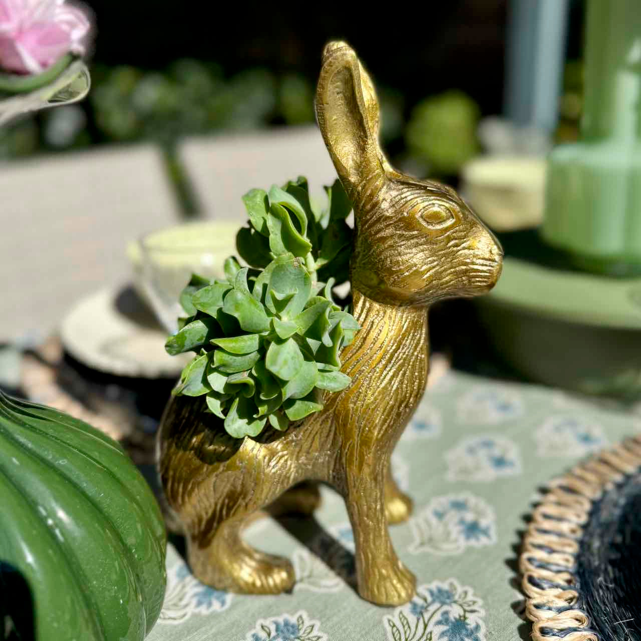 Gold rabbit-shaped planter with green succulents on a floral tablecloth.