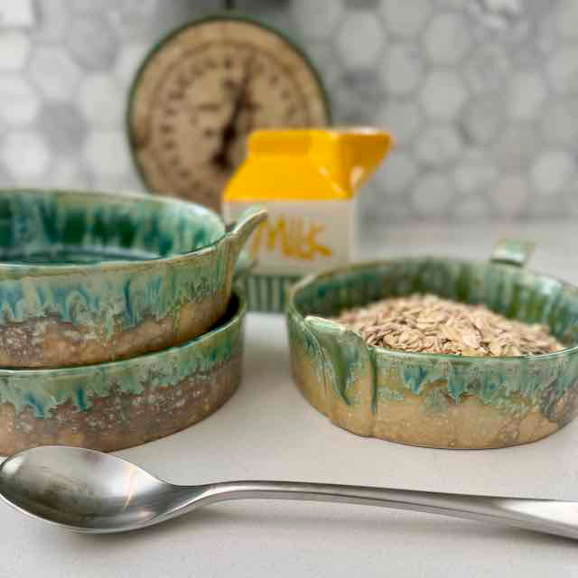 Set of ceramic bowls with green glaze on a white surface, with a carton of milk in the background.