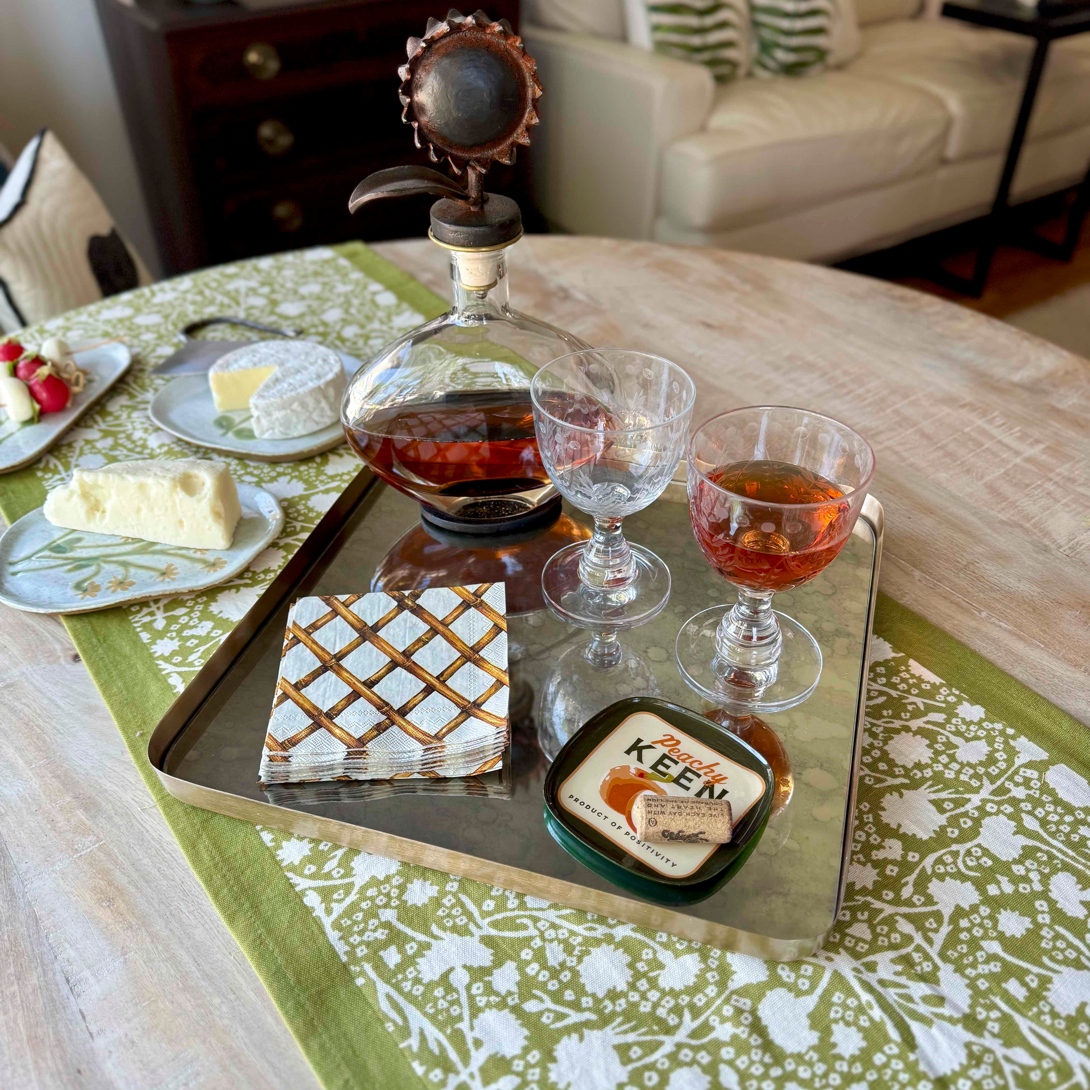 Decanter with glasses on a mirrored tray on a table with a decorative cloth.