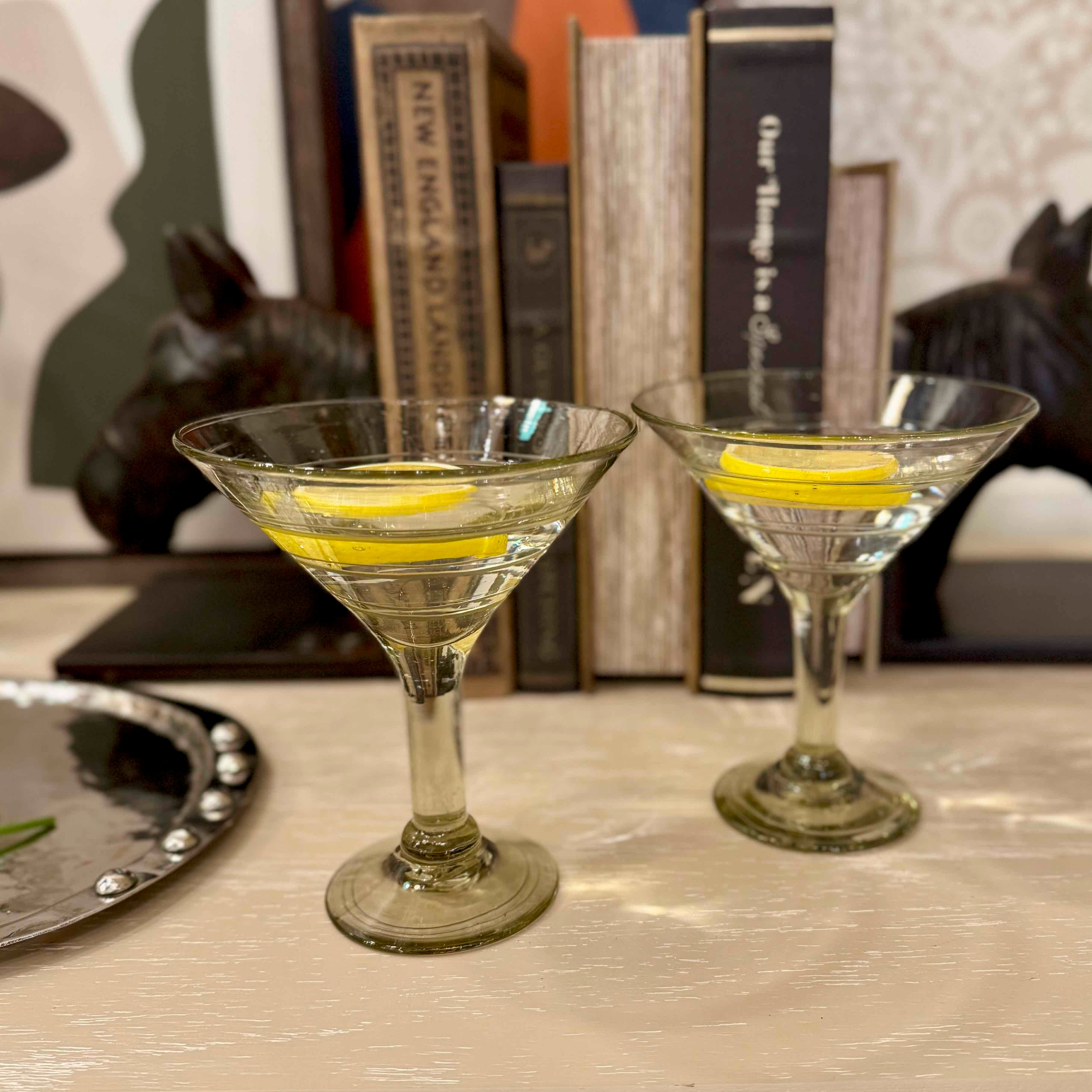 Two martini glasses with lemon slices on a table with books in the background
