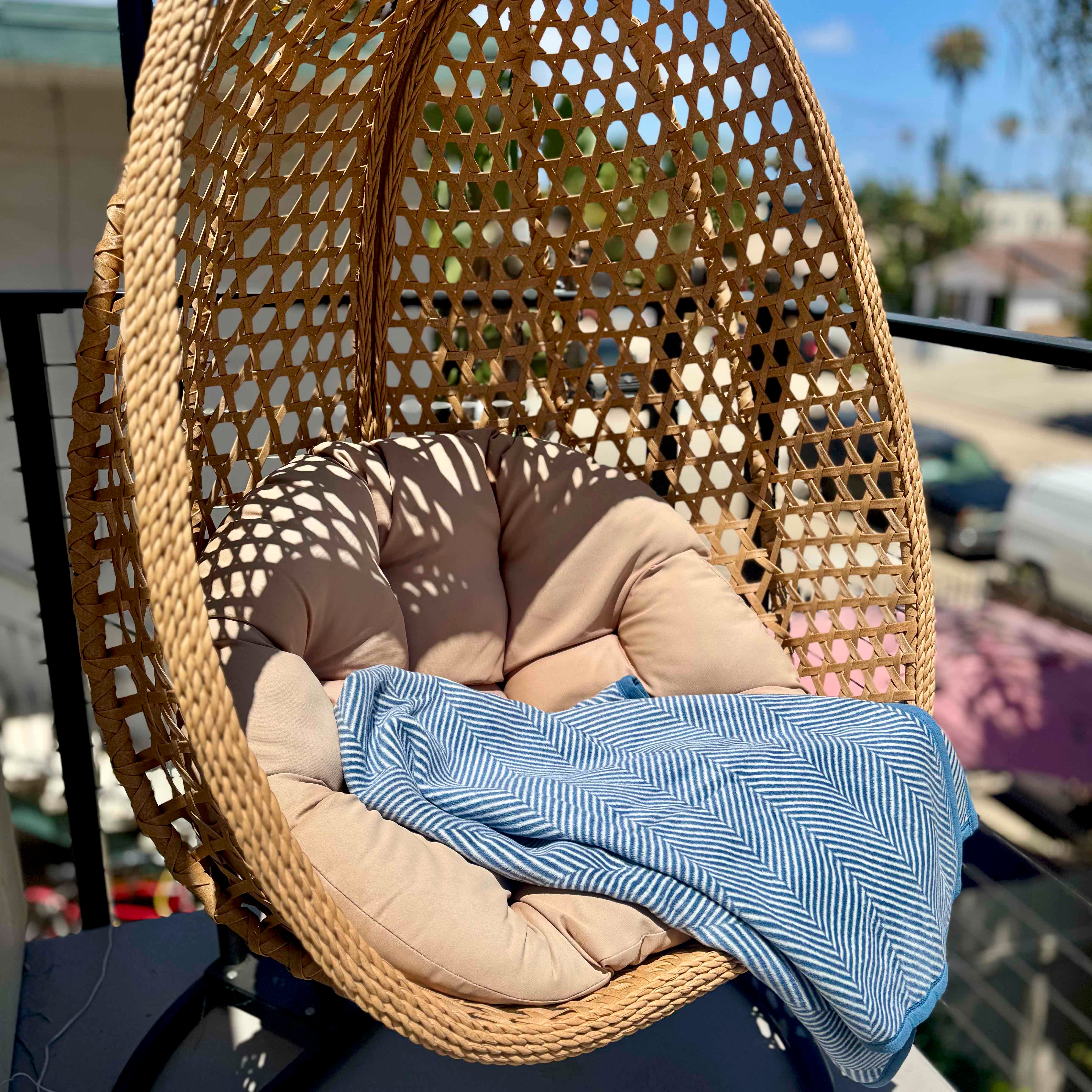 Wicker egg chair with cushions and a blanket on a balcony