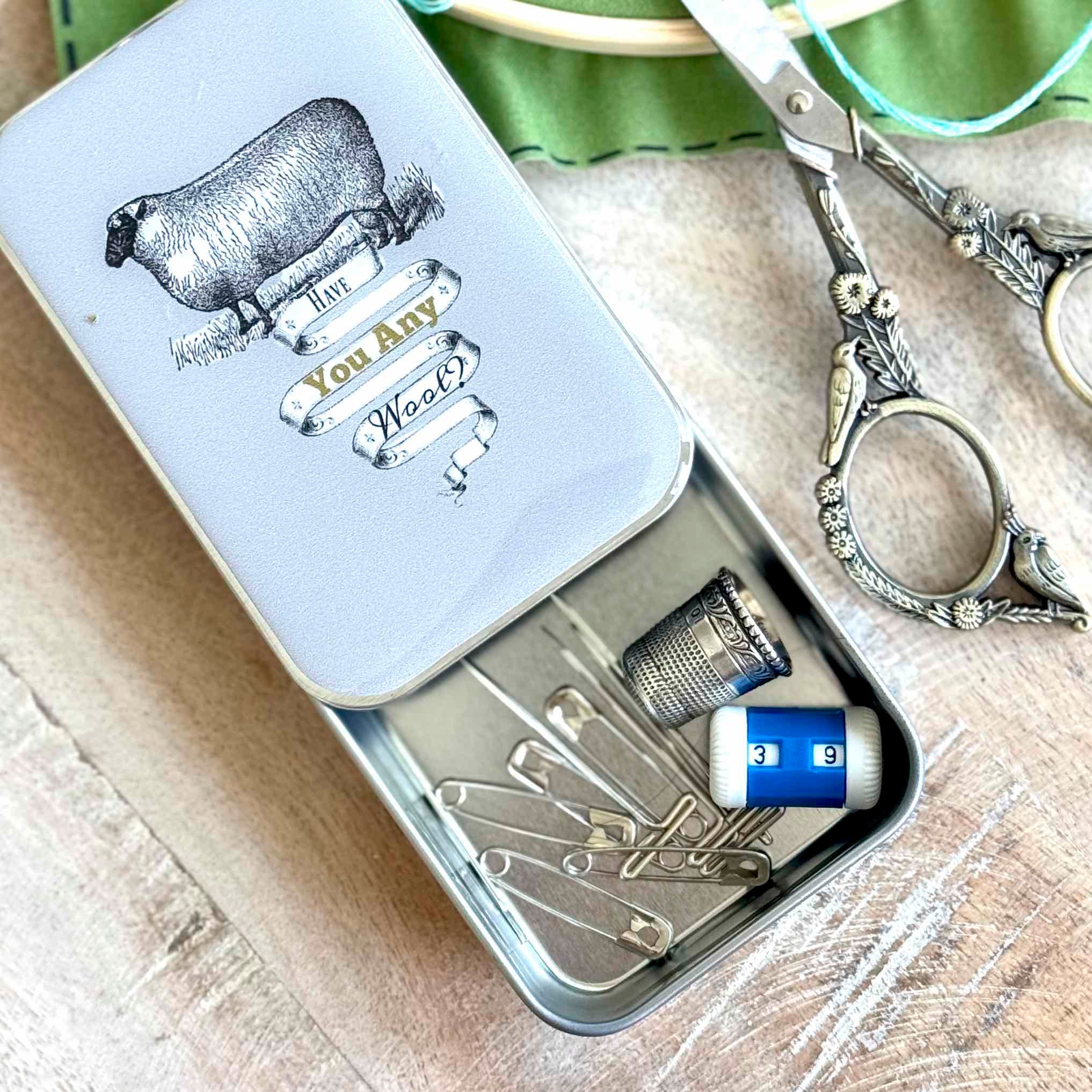 Small metal tin with sewing supplies including pins and a tube of cream, on a wooden surface.