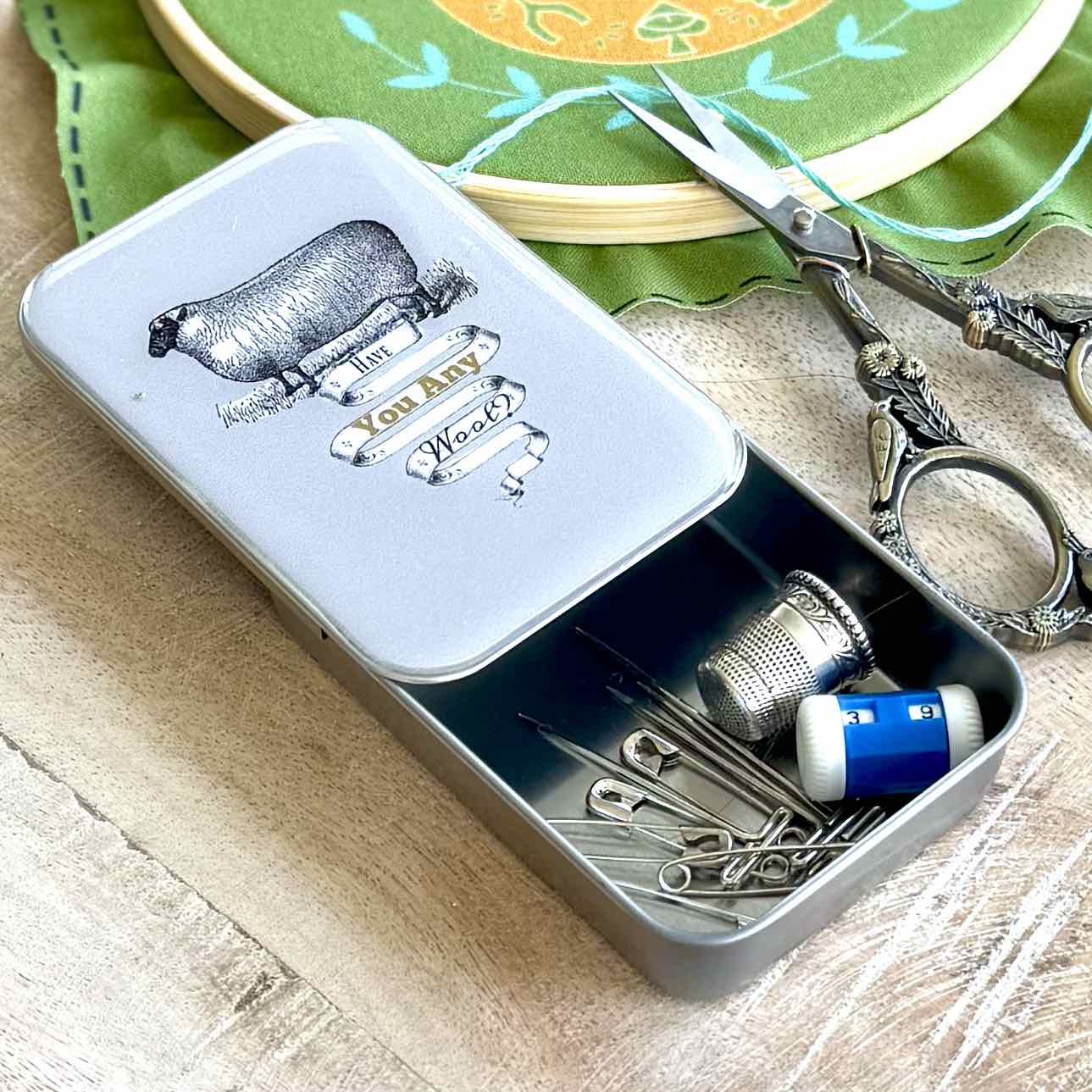 Small metal sewing kit with tools on a wooden surface