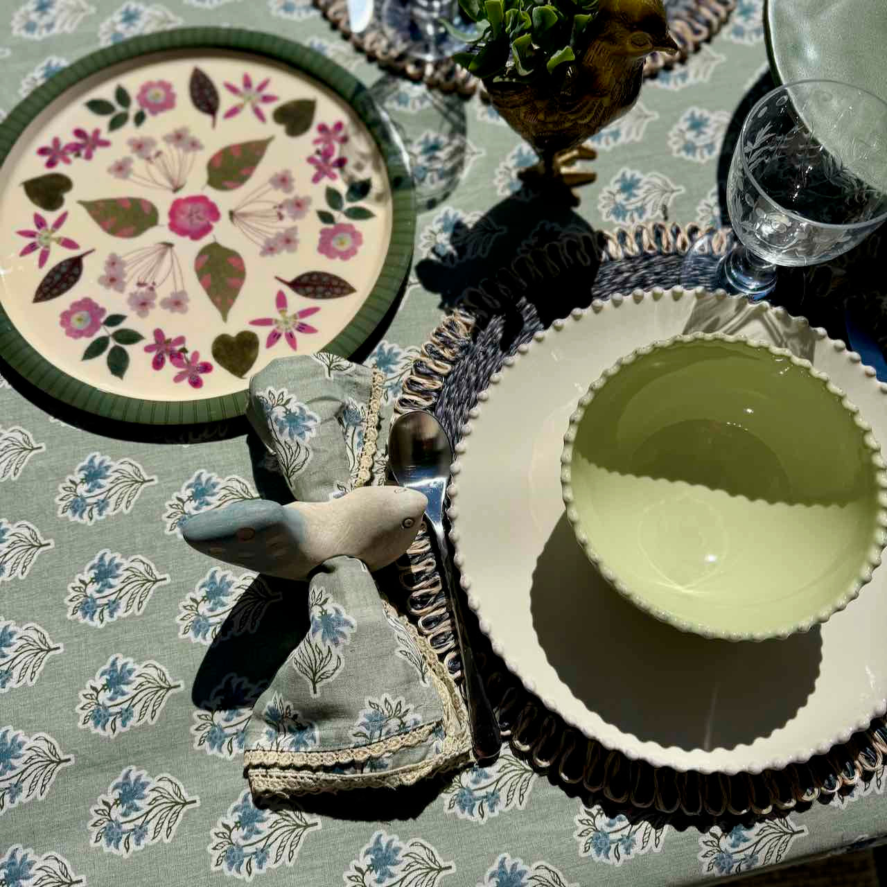 Decorative table setting with floral plates, napkins, and a glass on a patterned tablecloth.