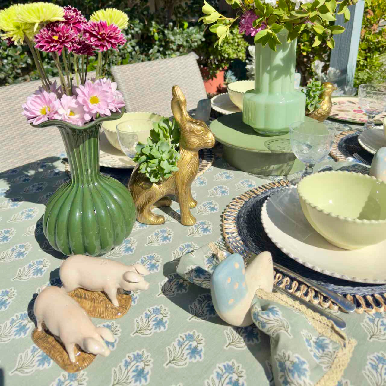 Decorative table setting with floral arrangements, animal figurines, and patterned tablecloth.