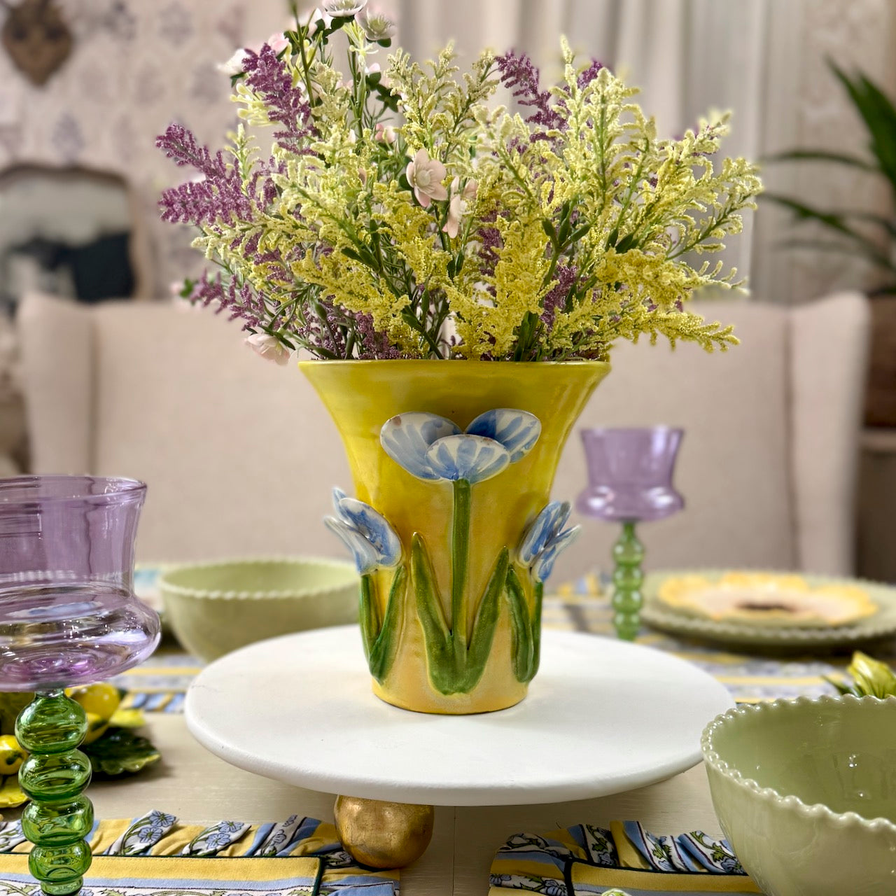 Decorative table setting with a yellow vase holding flowers on a white plate.
