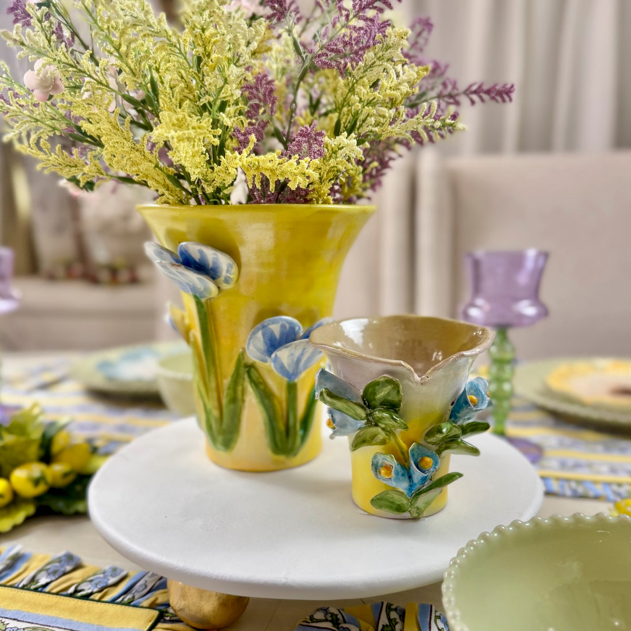 Decorative ceramic items including a yellow vase and small cup with floral designs on a table.