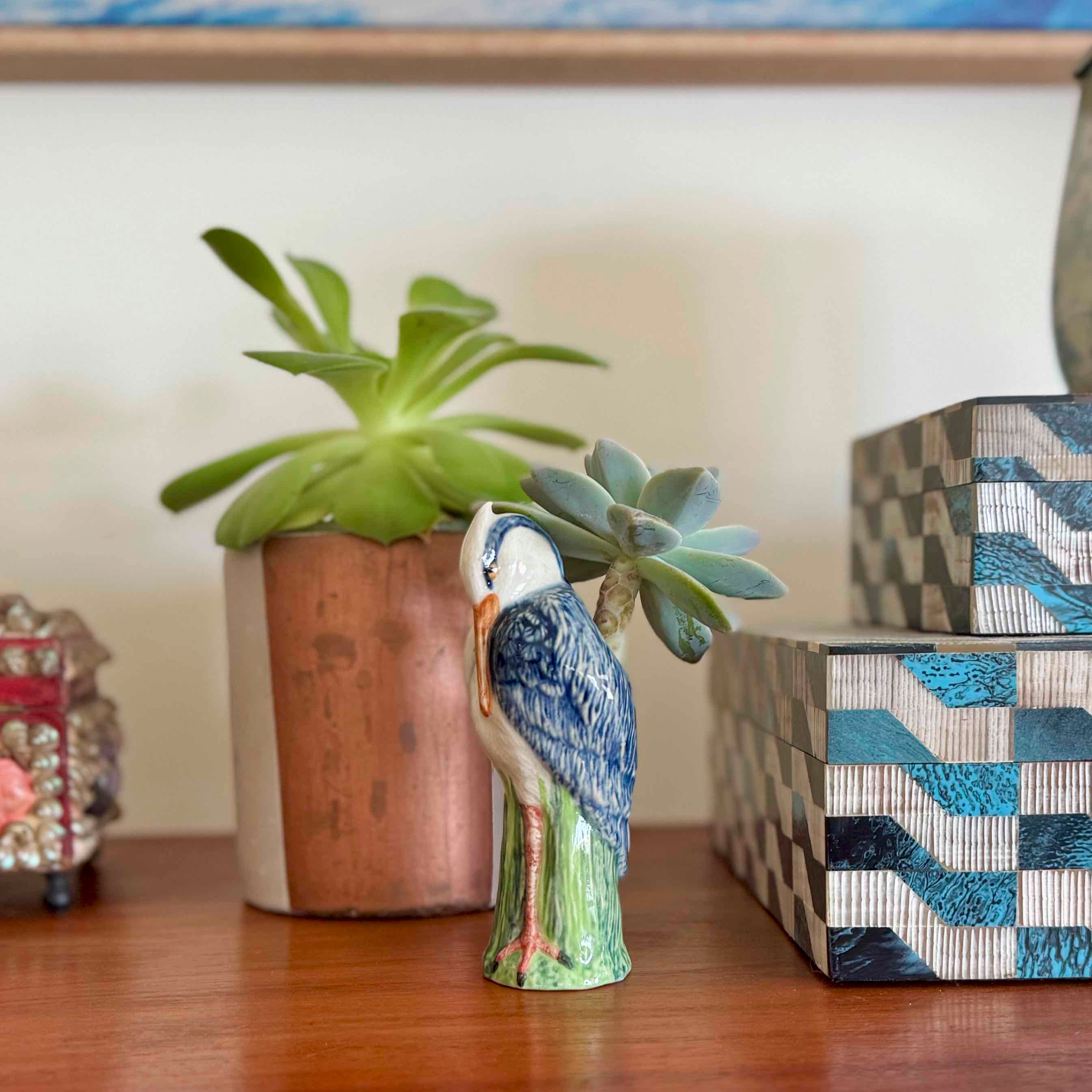 Decorative bird figurine, potted plant, and patterned box on a wooden surface.