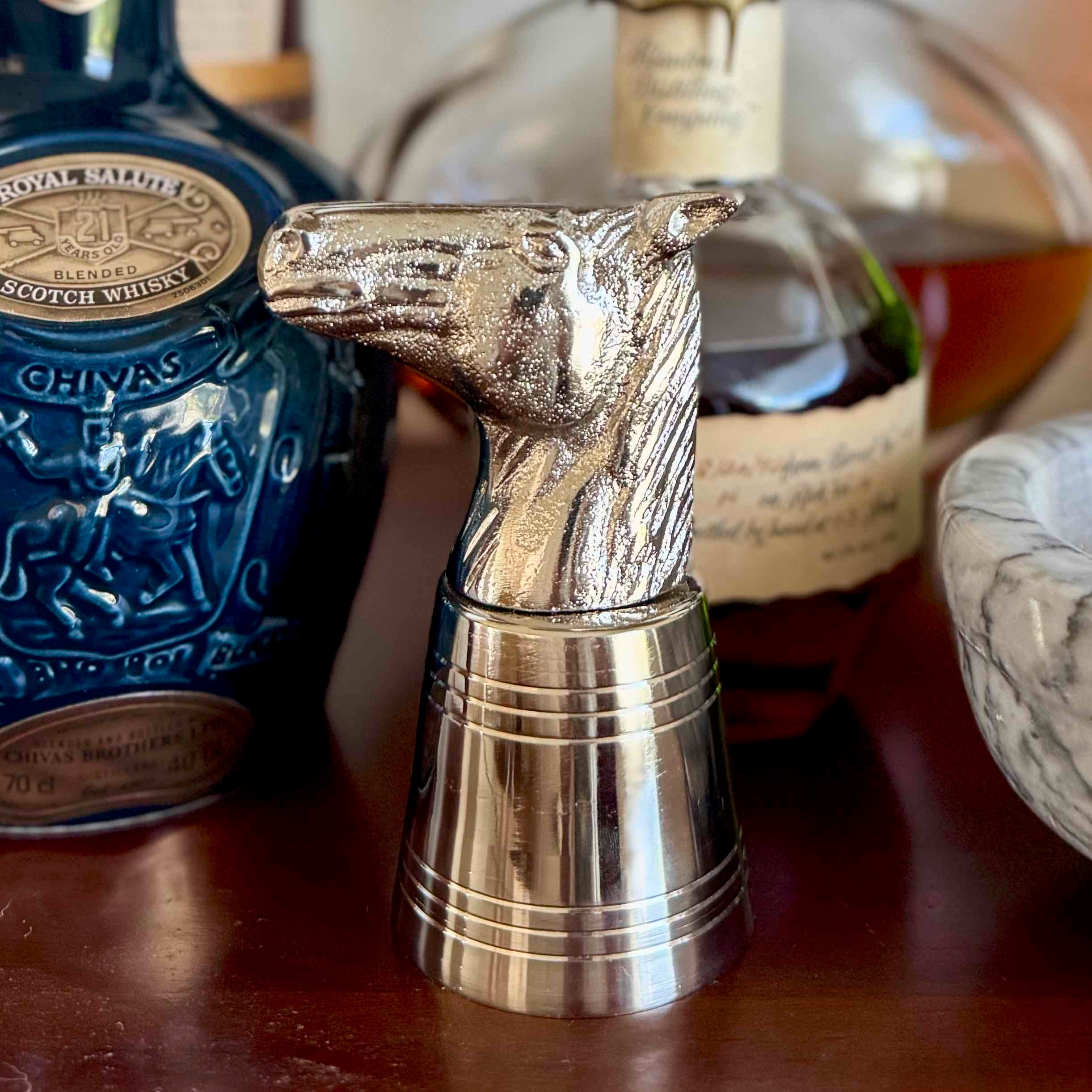 Metallic horse head decanter stopper with bottles in the background