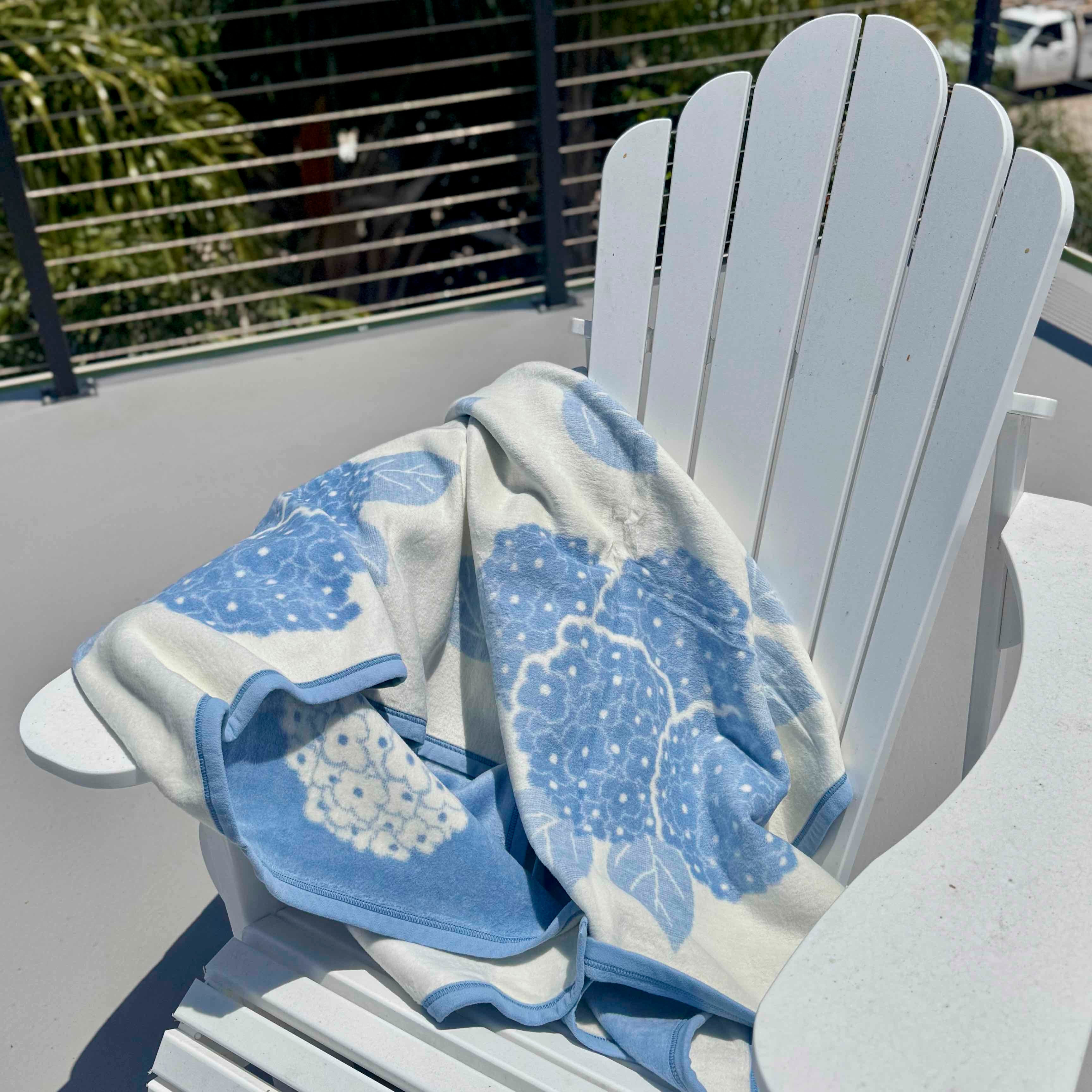 Blue and white floral-patterned towel draped over a white Adirondack chair outdoors.
