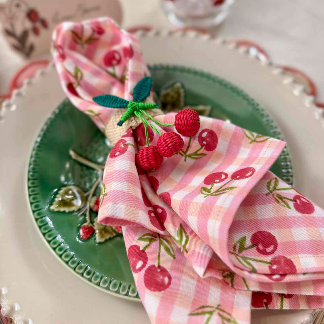 Decorative table setting with pink checkered napkin and cherry design on a green plate.