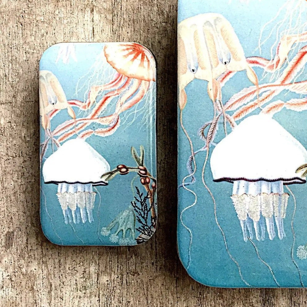 Two rectangular metal coasters with rounded corners featuring a whimsical jellyfish ocean illustration, displayed on a rustic wooden surface.