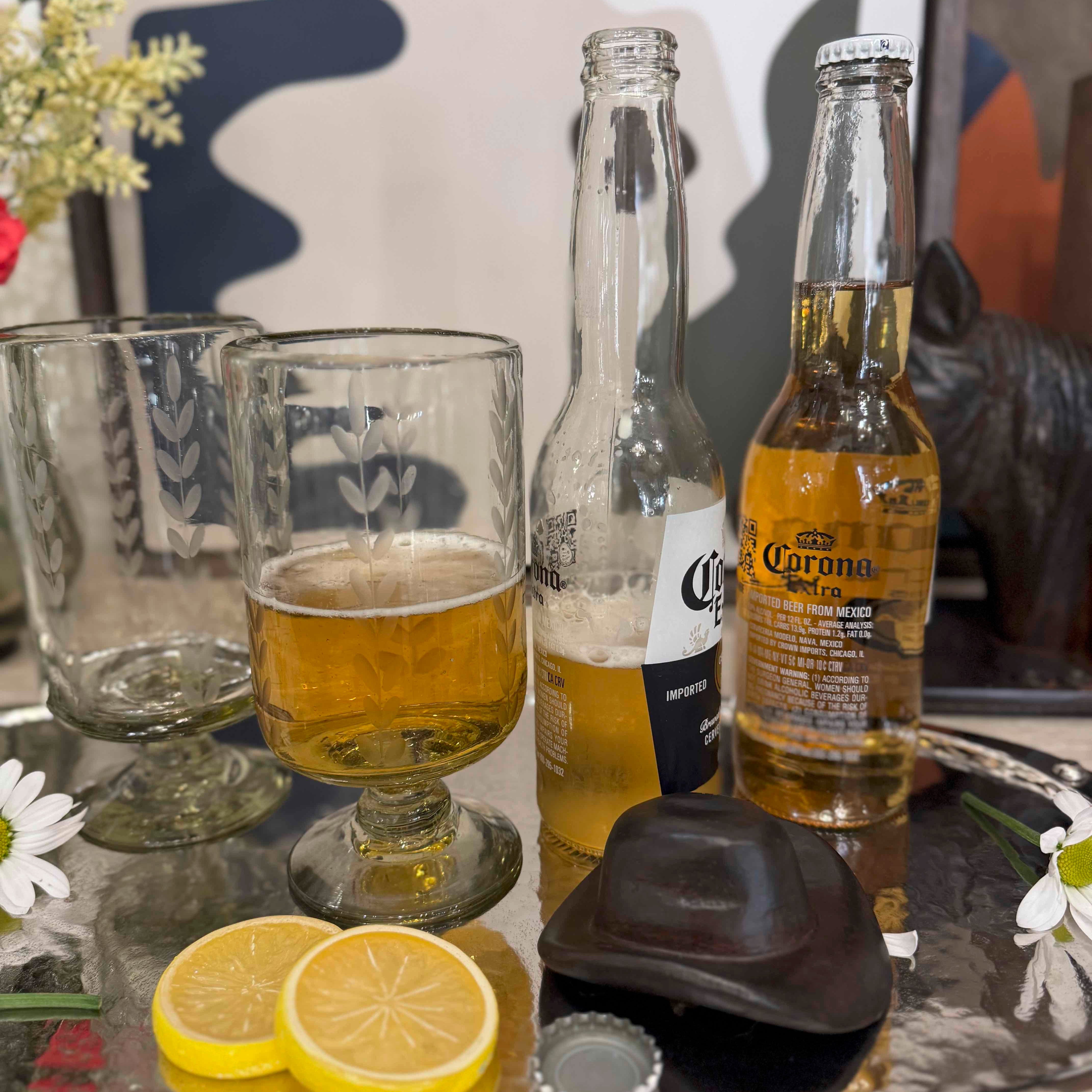 Tray with Corona beer bottles, glasses, lemons, and a chocolate bar on a decorative background.