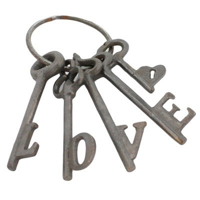 A set of four vintage-style metal keys on a split ring, arranged to spell out the word LOVE, on a plain white background.