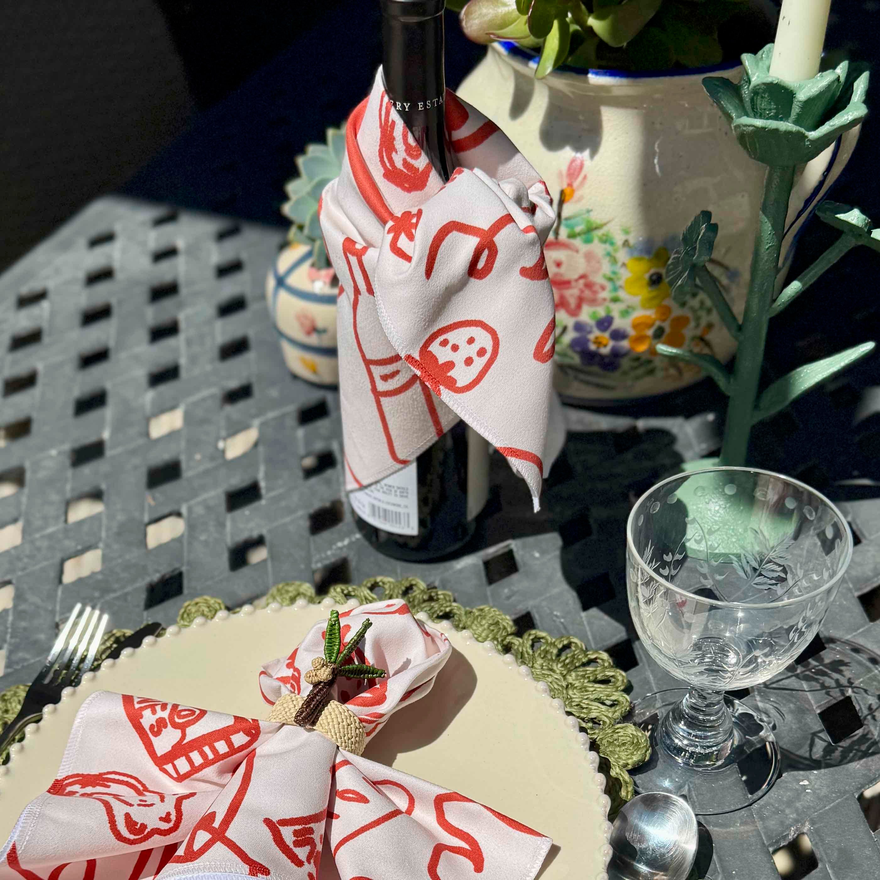 Wine bottle with decorative napkin on a table with a glass and other items.