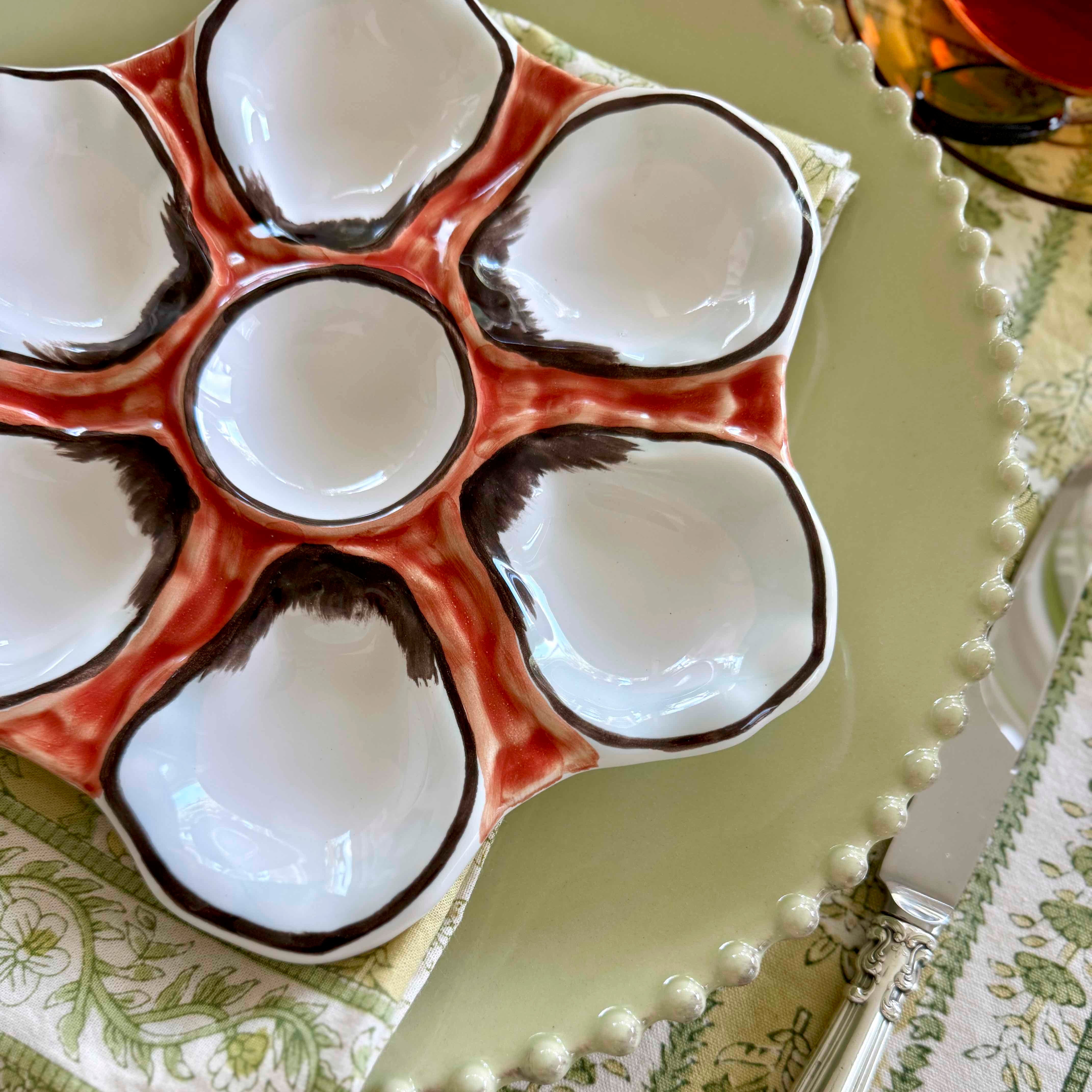 Decorative ceramic oyster plate with white bowls on a green tablecloth.