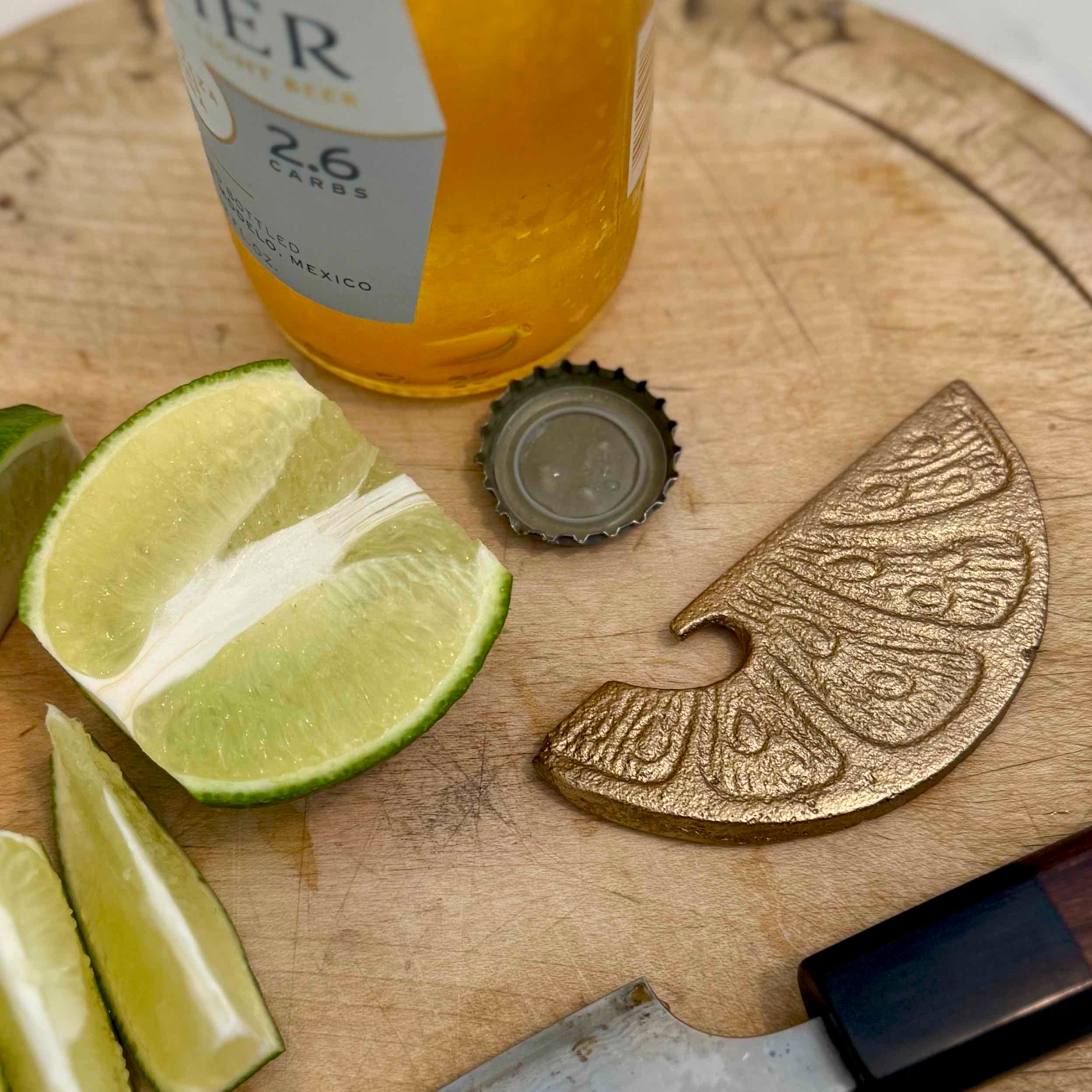 Bottle of beer with lime wedges and a decorative metal object on a wooden surface