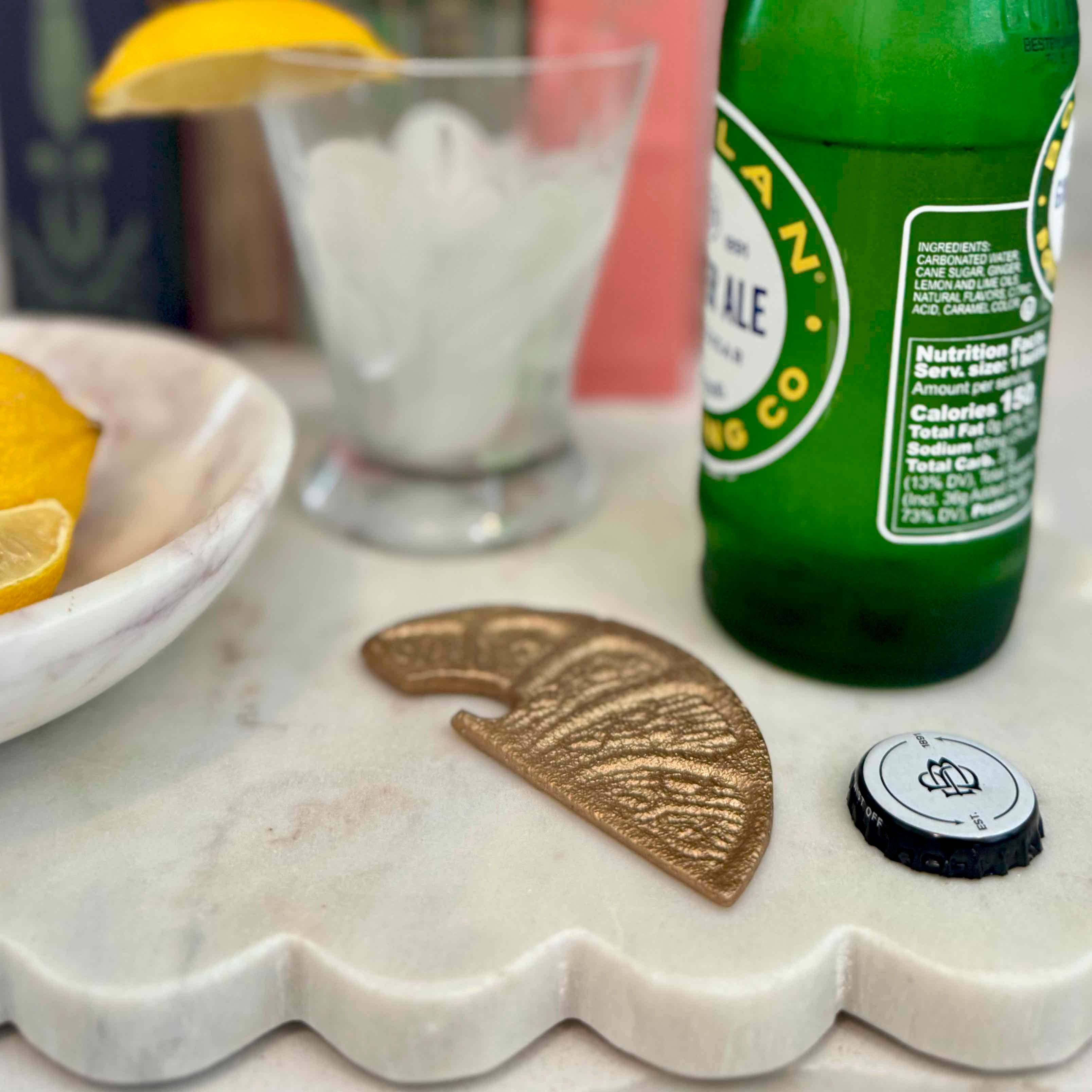 Green bottle of Heineken beer on a marble surface with lemons and a glass in the background.