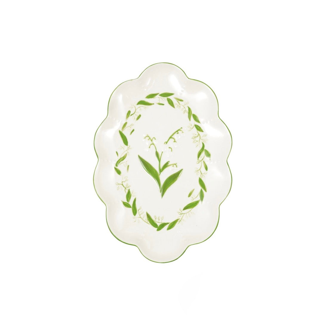 An oval ceramic serving platter with scalloped edges, featuring a green lily of the valley floral design on a white background.