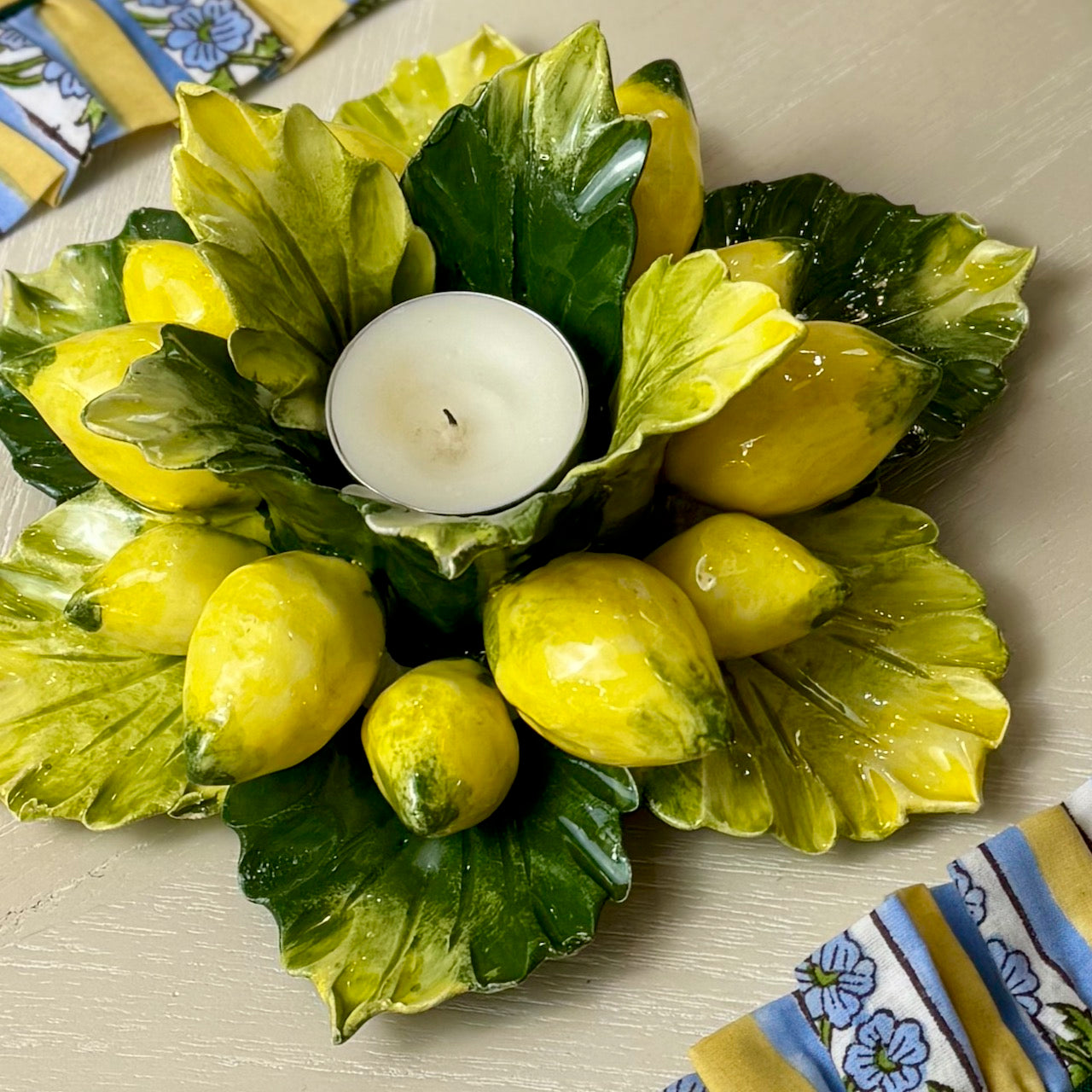 Decorative candle holder with lemons and green leaves on a light surface